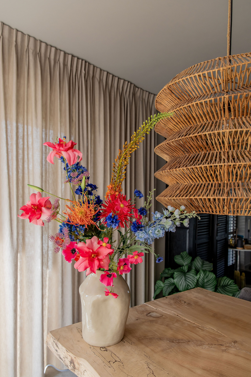 Vrolijk zomerboeket van zijden bloemen in een crèmewitte vaas met organische vorm op een houten tafel. Roze lelies springen eruit tussen blauwe en lic