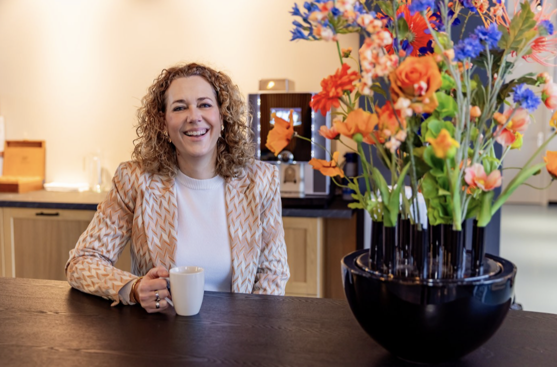 Santine aan tafel met een kop koffie naast een kleurrijk zijden boeket