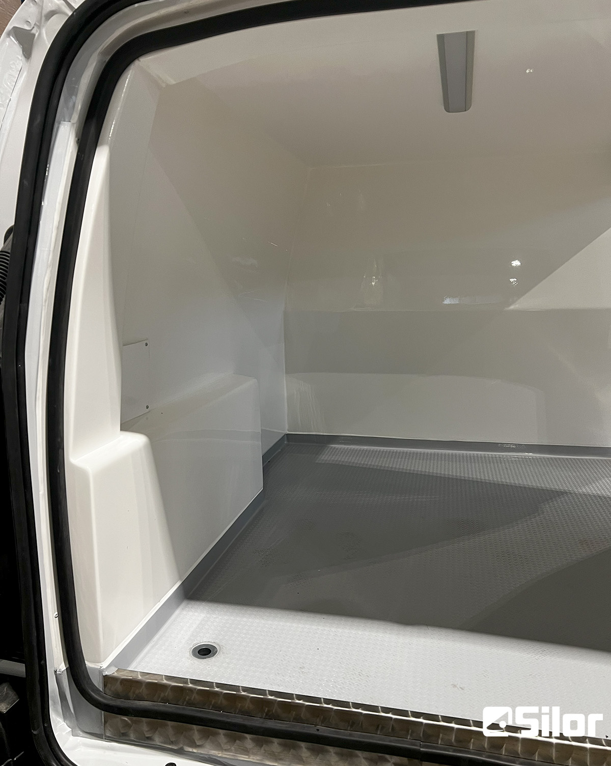 Interni di un veicolo commerciale con pavimento grigio e pareti bianche.