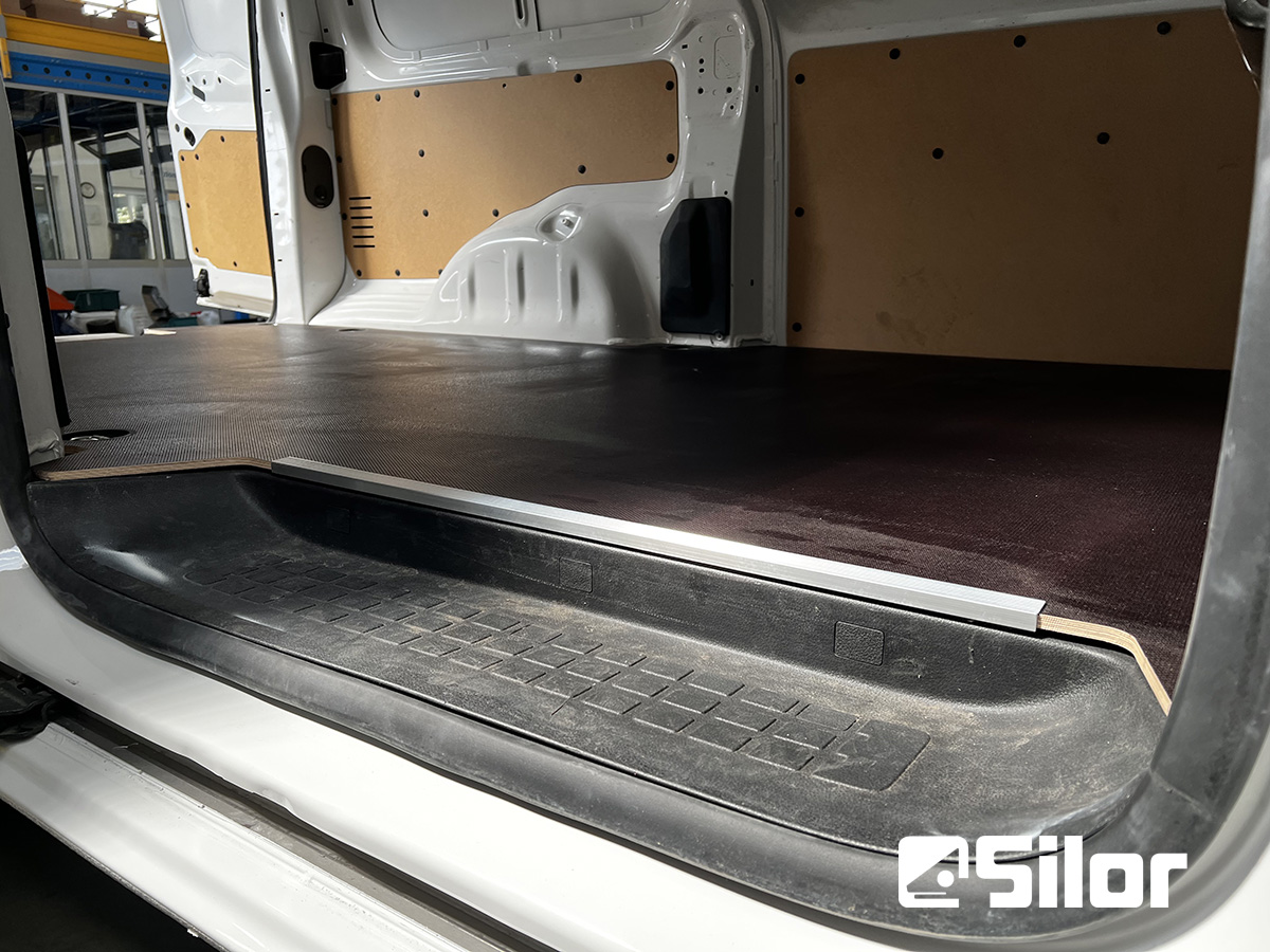 Interni di un furgone cargo bianco con pareti in legno e pavimento nero.