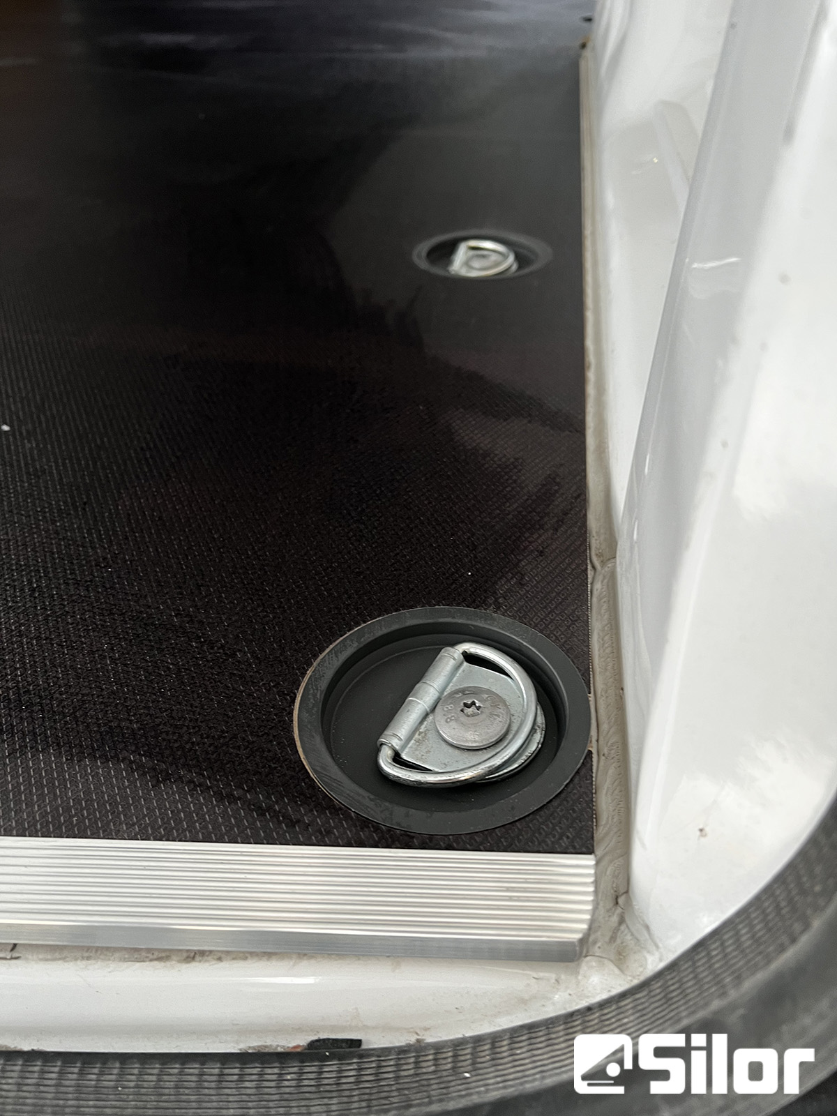 Vista ravvicinata di un anello di ancoraggio a D in metallo su un pavimento nero in un furgone.