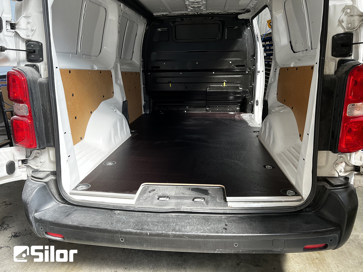 Interni di un furgone bianco con pavimento nero e pannelli marroni.