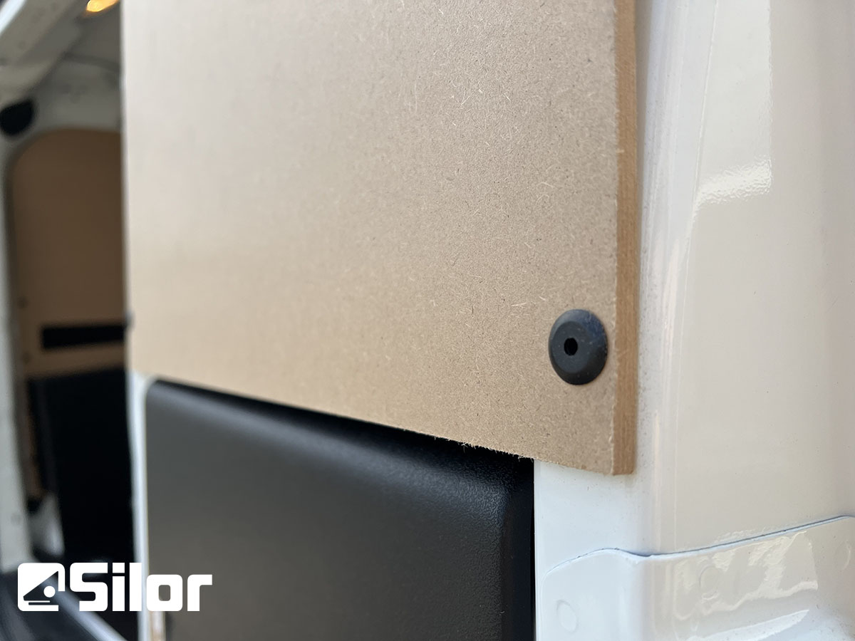 Un pannello di legno chiaro fissato al rivestimento interno di un furgone bianco con un fermo nero.