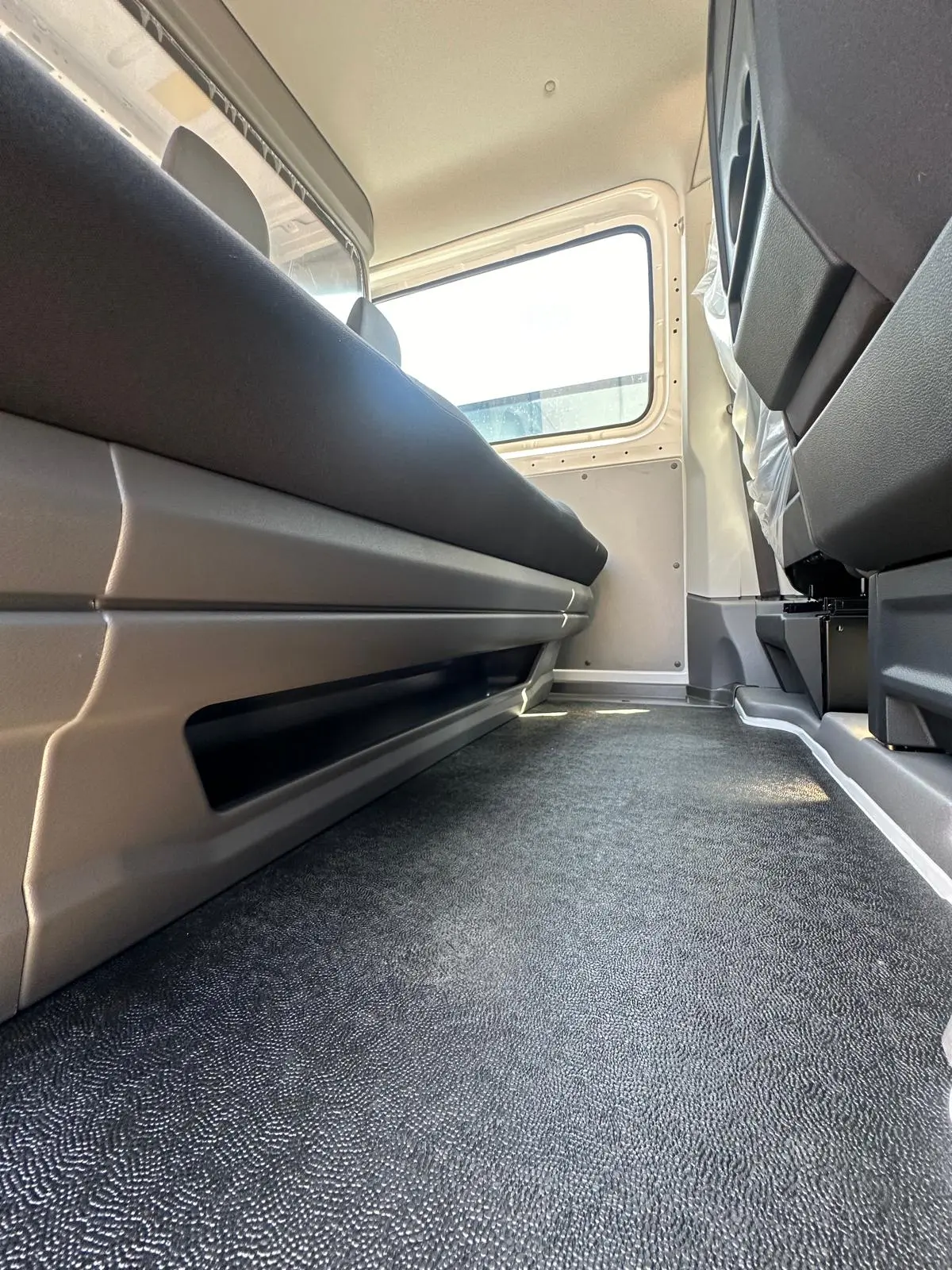 Interni spaziosi con pavimento testurizzato, sedili grigi e spazio di archiviazione.
