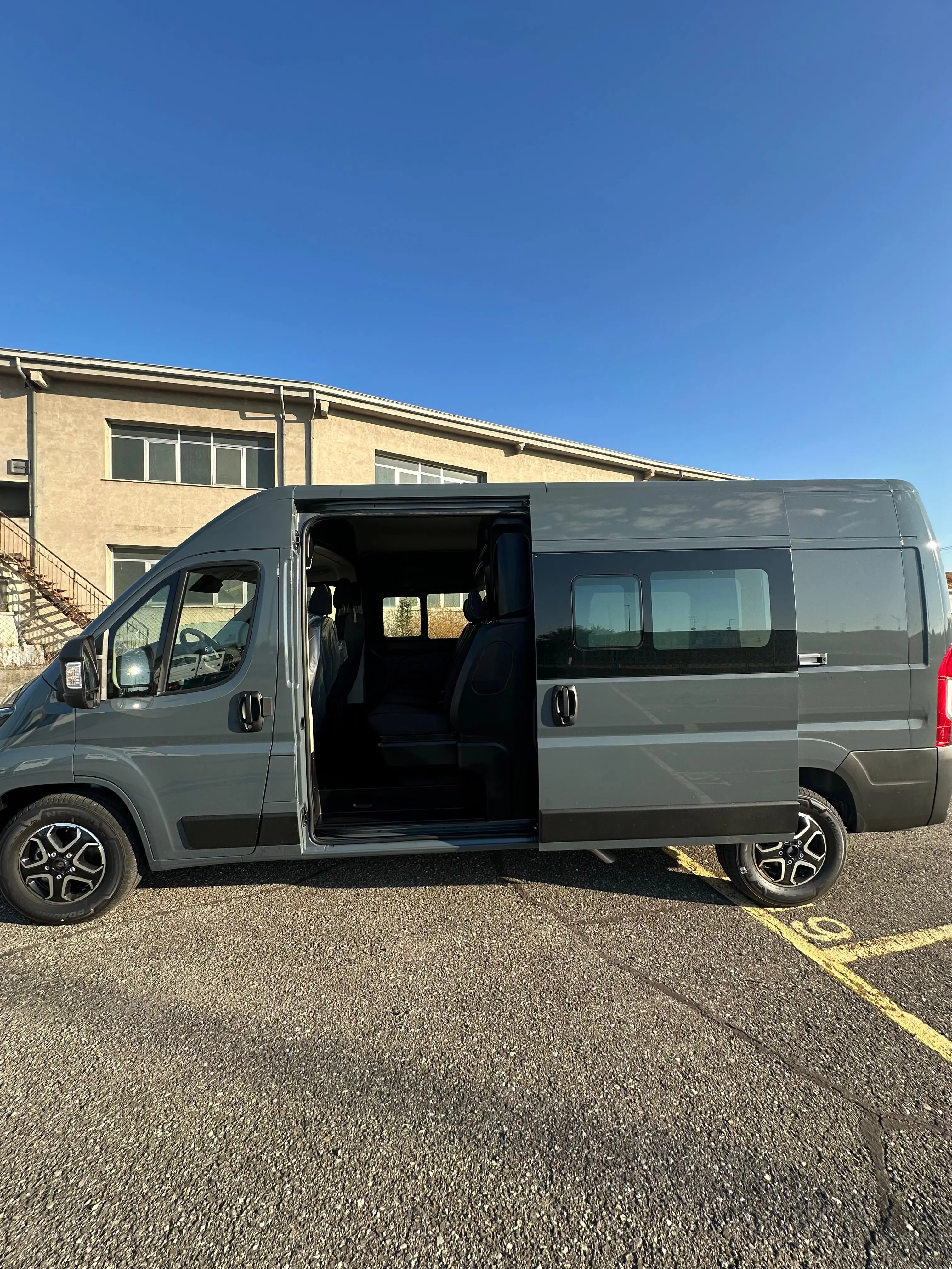 Un furgone grigio con una porta scorrevole aperta parcheggiato su un parcheggio asfaltato.