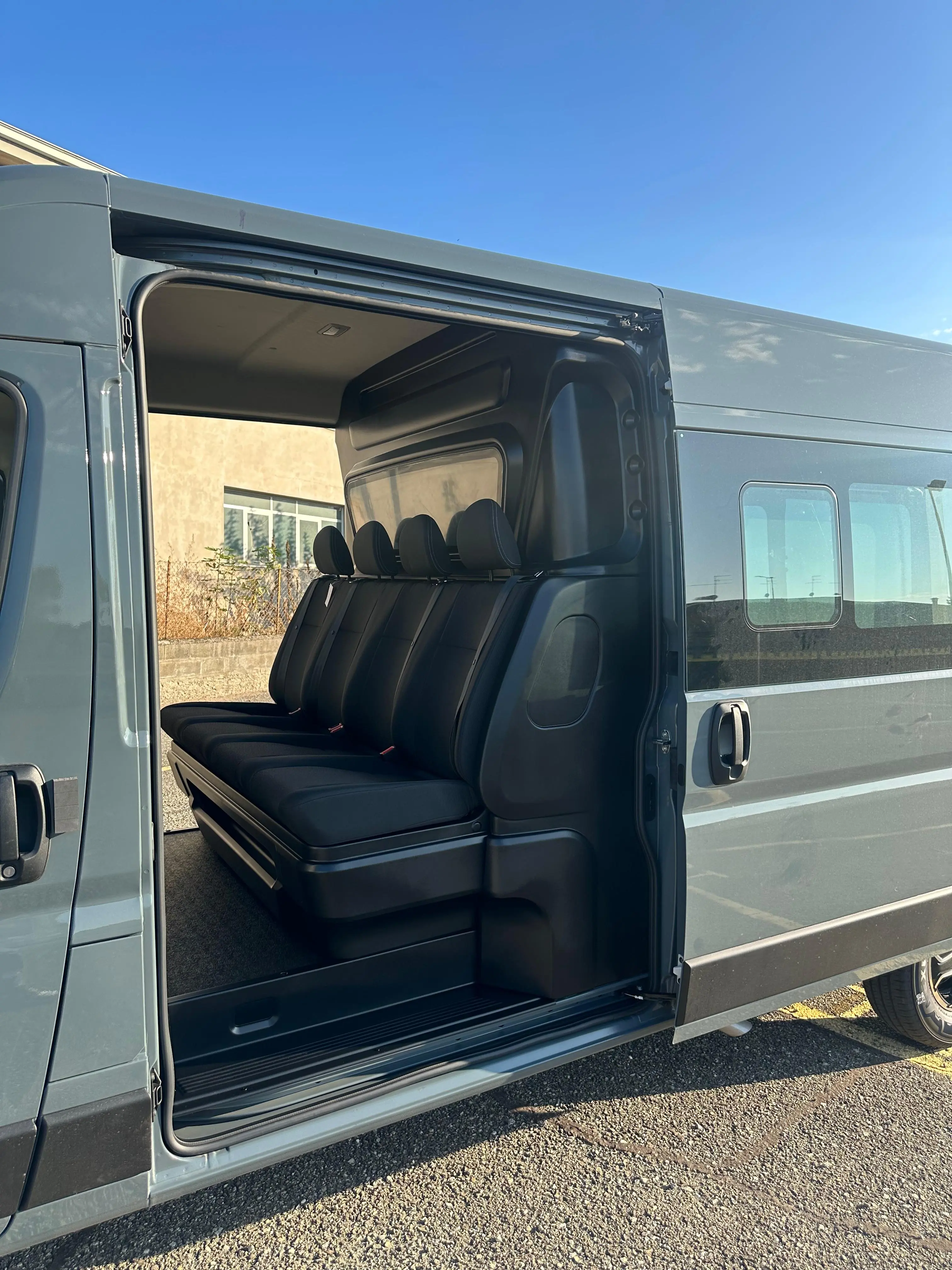 Interno di un furgone passeggeri con sedili neri, con la porta scorrevole aperta.