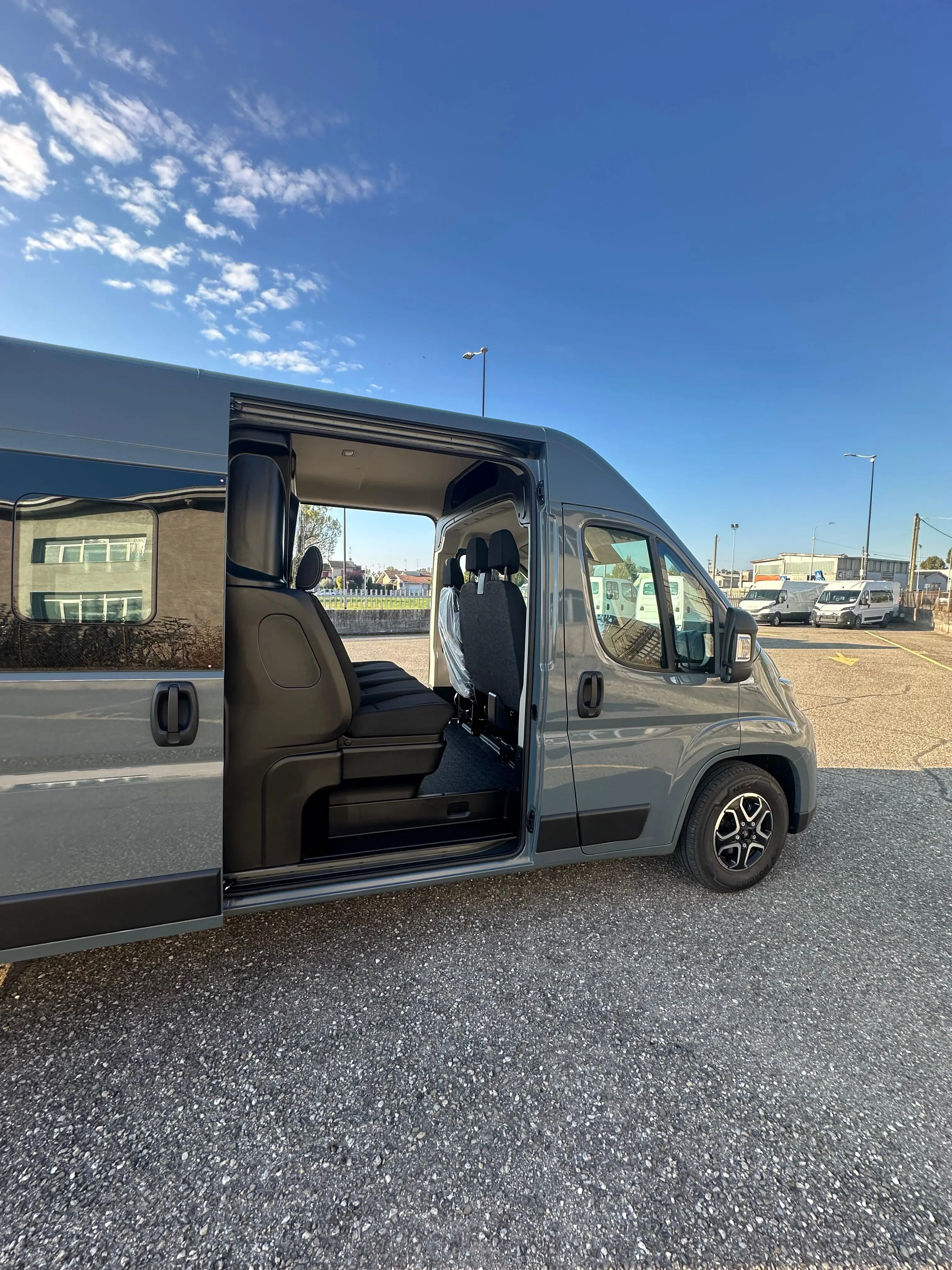 Van grigio con portiera scorrevole aperta su parcheggio asfaltato. Cielo blu con nuvole.