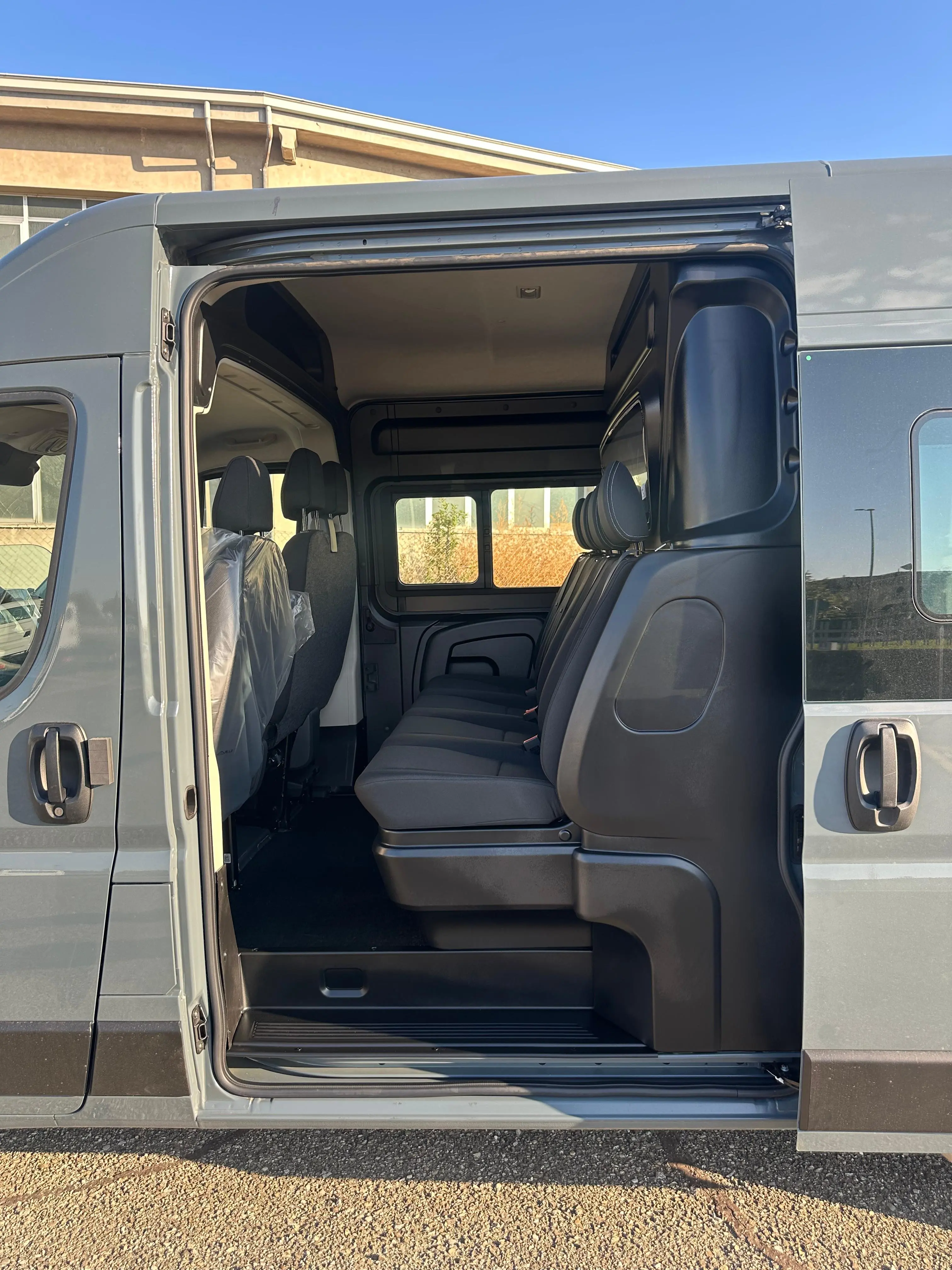 Interni di un furgone passeggeri grigio con sedili imbottiti neri e rivestimenti in plastica.