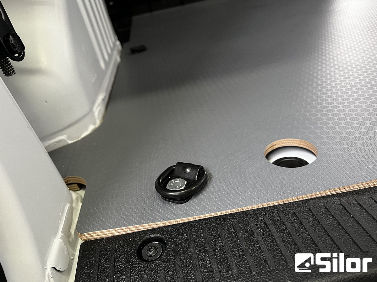 Interni di furgone modernizzati con pavimento in legno grigio e elementi di fissaggio neri.