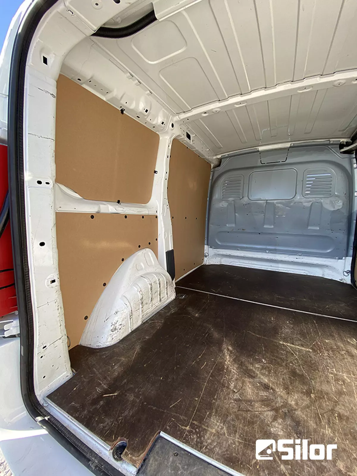 Interno furgone bianco con pannelli in legno e pavimento scuro.