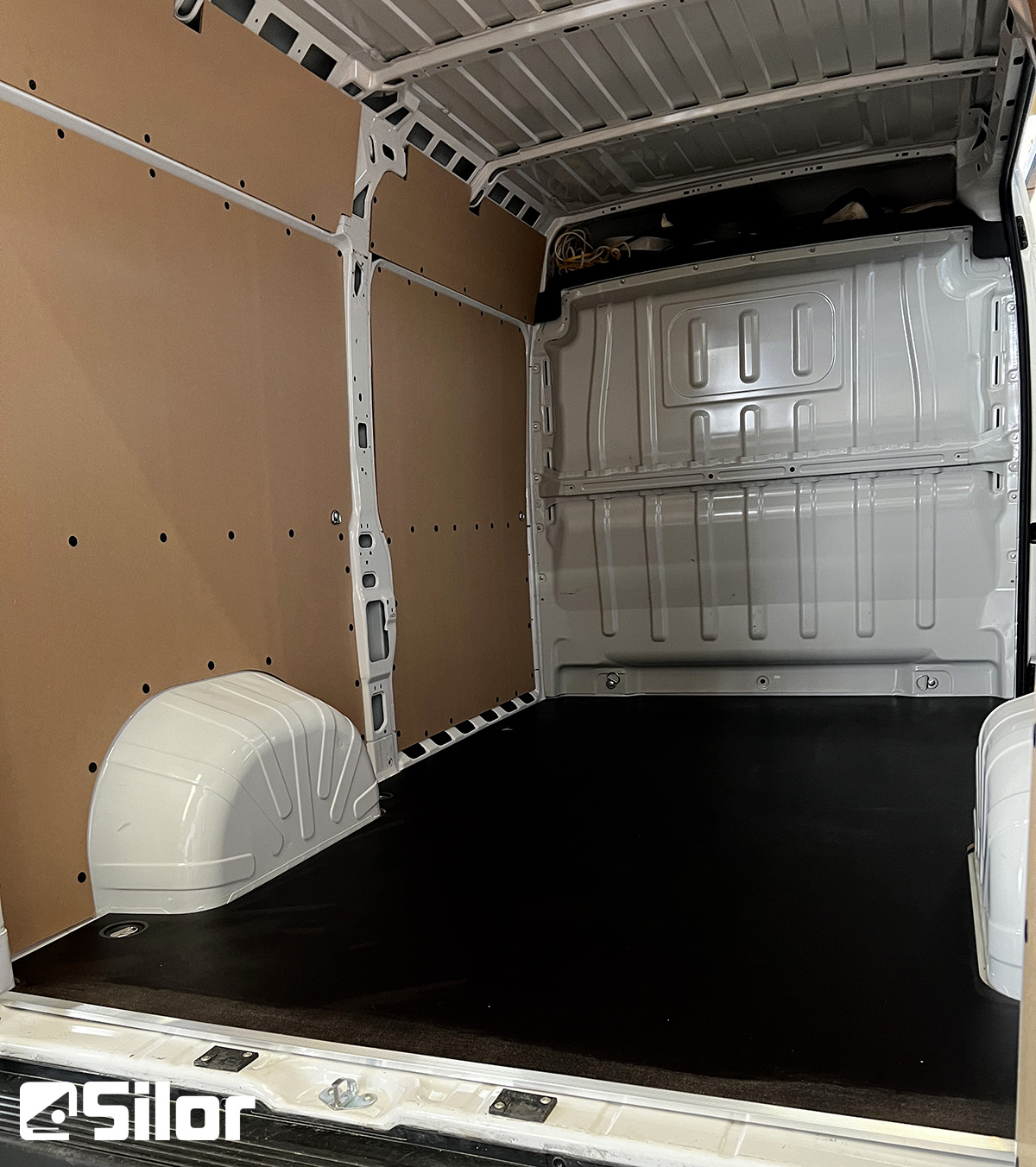 Interni di furgone con pavimento nero e pareti marroni.