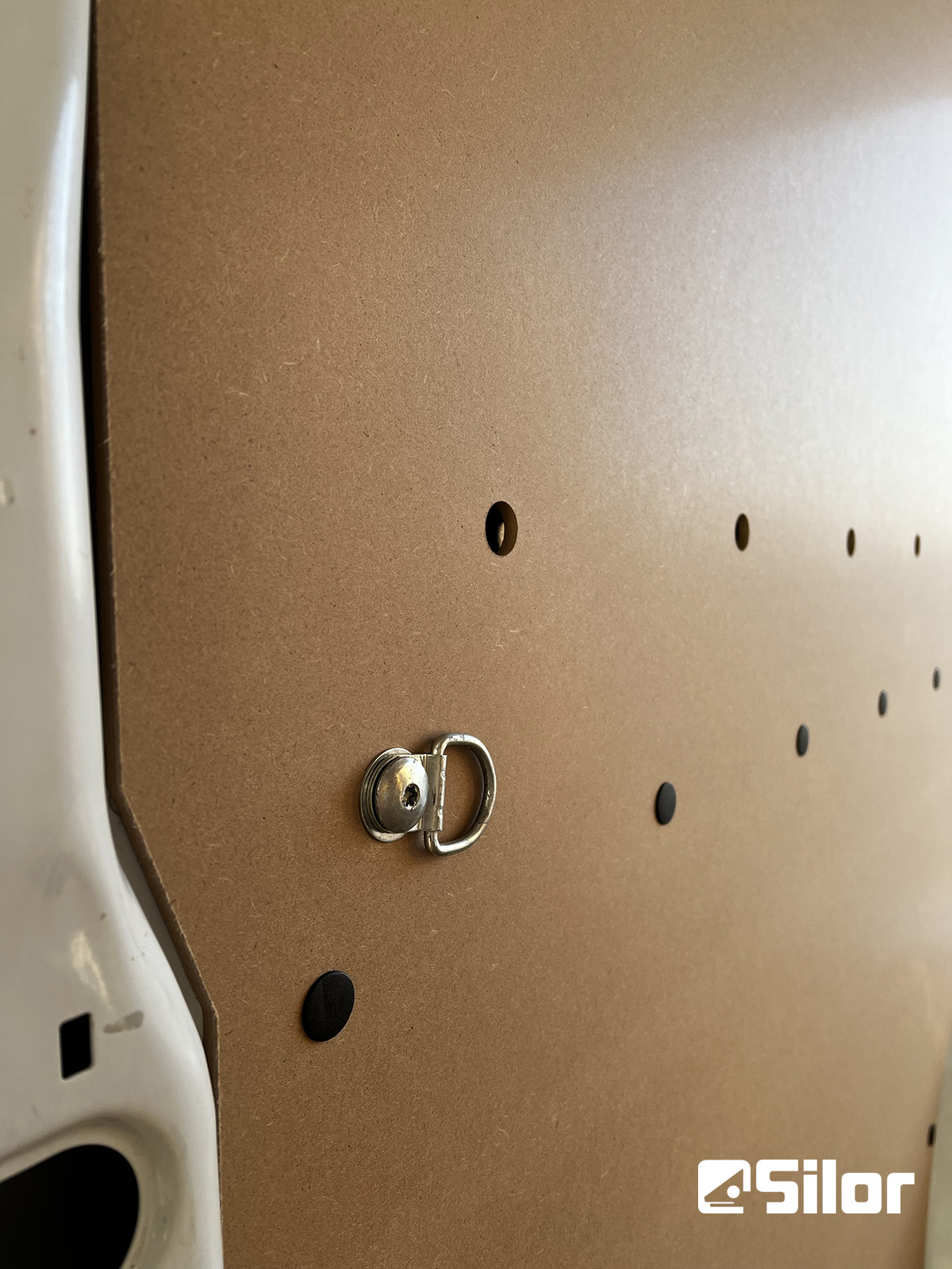 Una parete di compensato con un anello a D e piccoli fori.