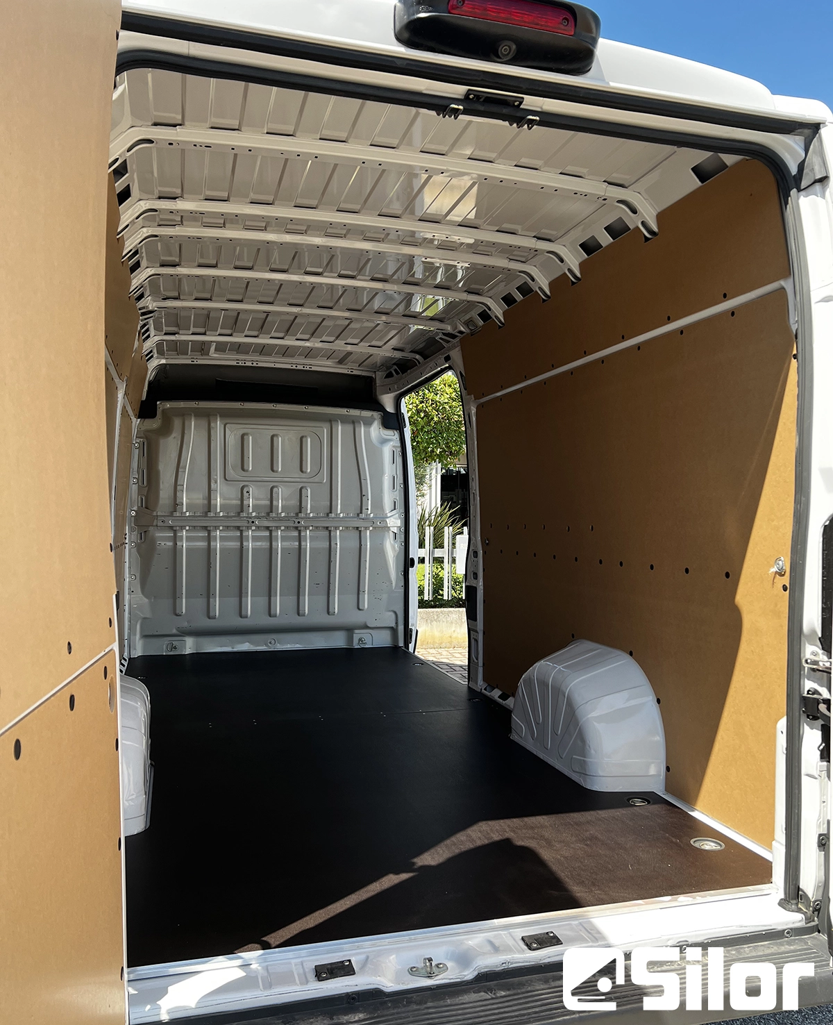 Interni di un furgone bianco con pavimento e rivestimenti marroni.