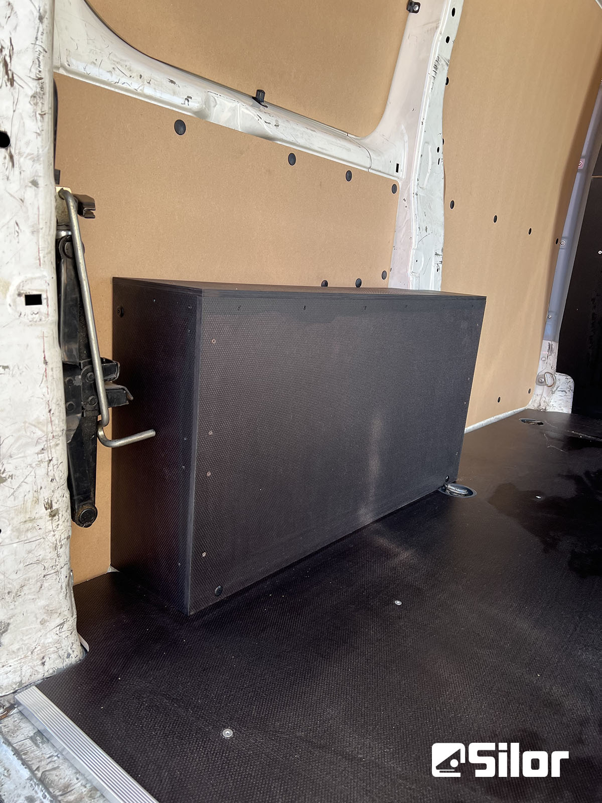 Interno di un furgone con rivestimenti in legno chiaro e una scatola nera sul pavimento nero.