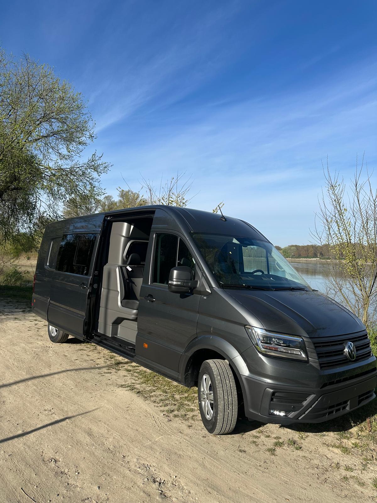 Un furgone grigio su una strada sterrata di fronte all'acqua con la portiera scorrevole aperta.