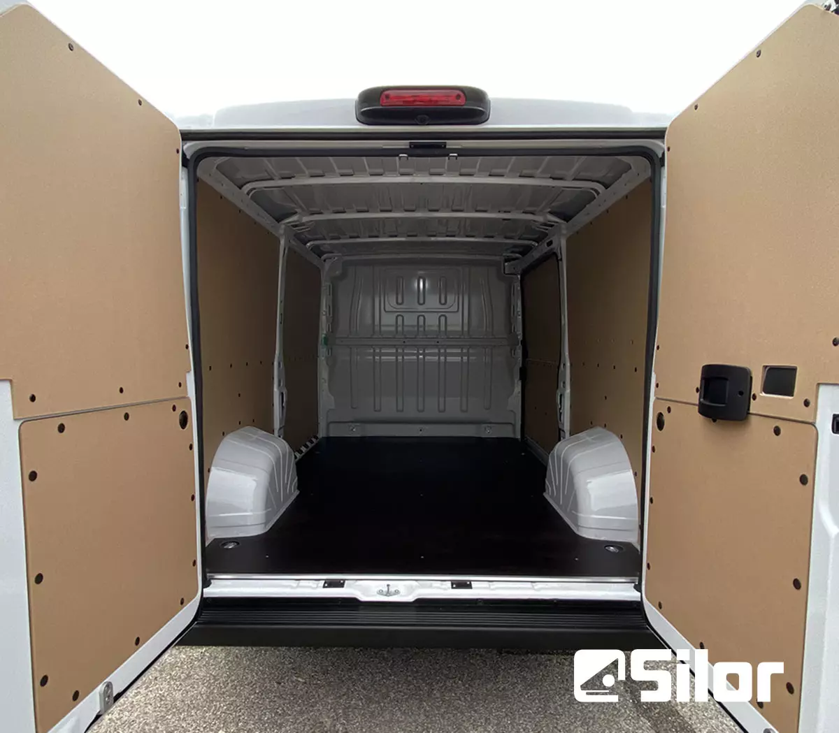 Interni di un furgone bianco con porte posteriori aperte, pareti interne color marrone chiaro e pavimento nero.