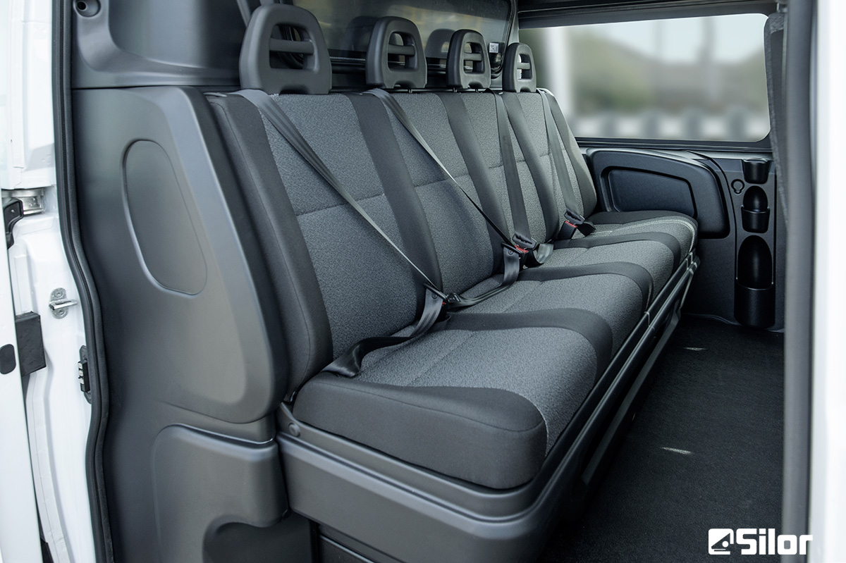 Interno furgone: fila di sedili grigi imbottiti con schienali alti e poggiatesta.
