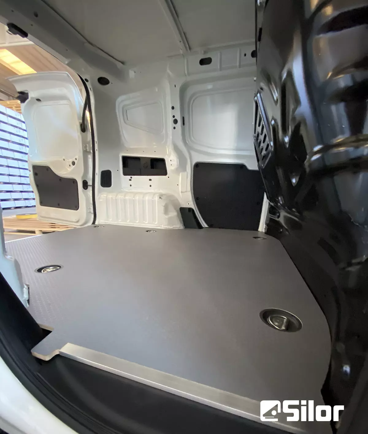 Interno di un furgone bianco con un pavimento di legno grigio chiaro.
