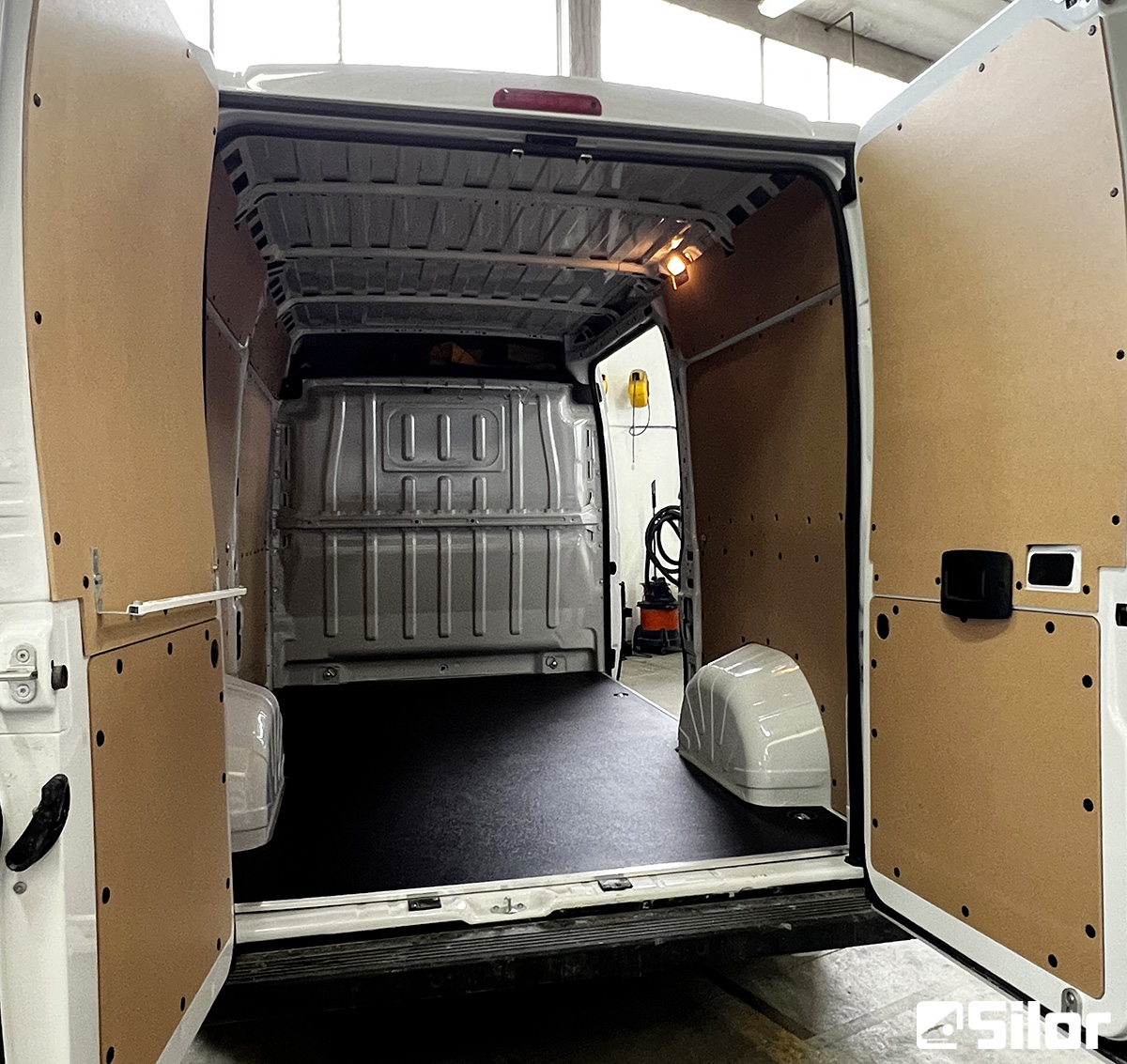 Interni di furgone bianco con porte posteriori aperte e pannelli di legno sui lati.