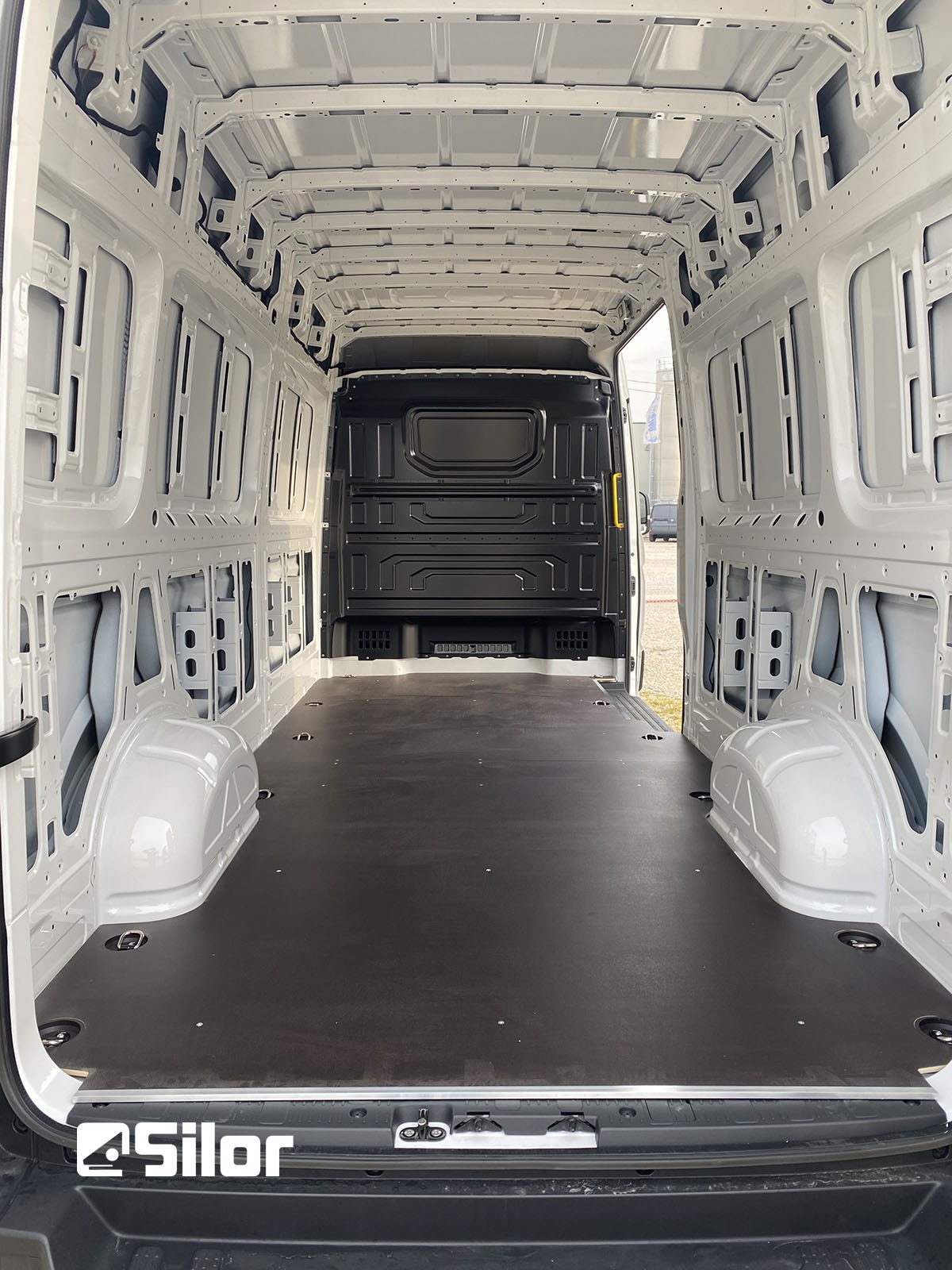 Interno spazioso di un furgone bianco con pavimento in legno scuro.