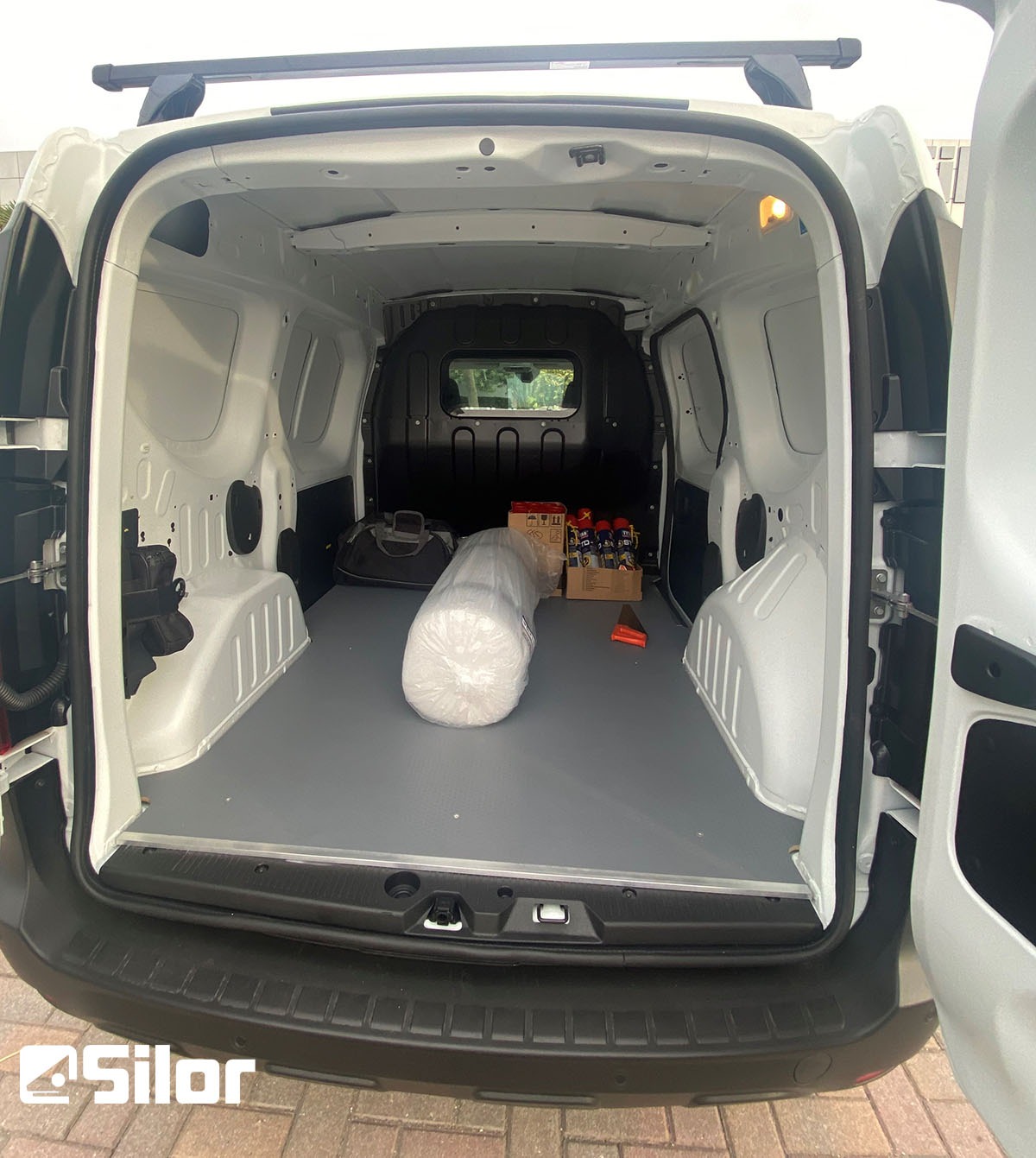 Interno di un furgone bianco con pavimento grigio e vari oggetti all'interno.