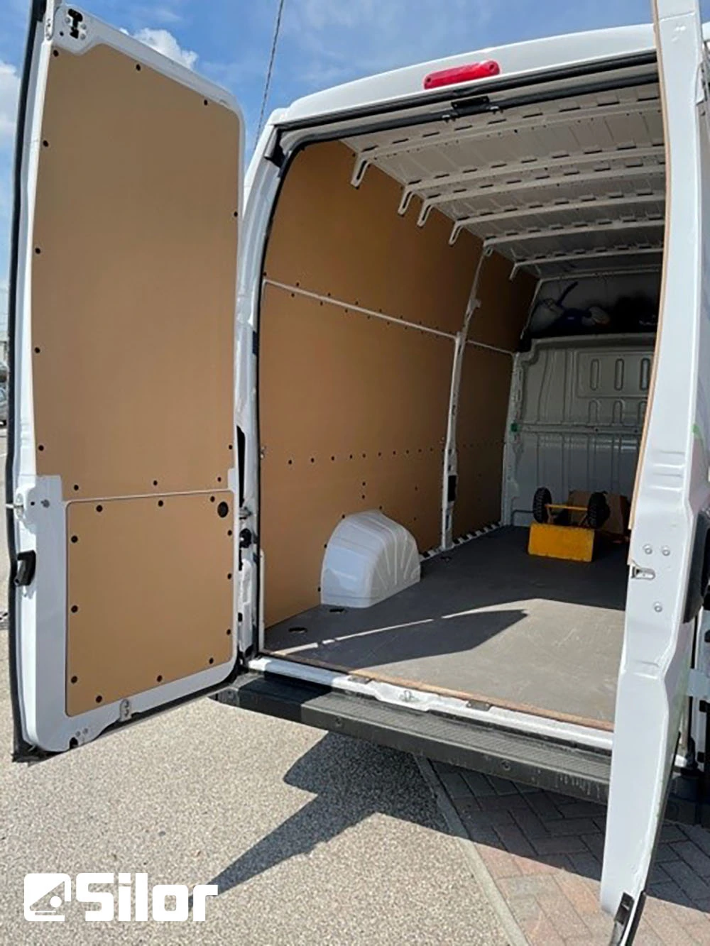 Interni spaziosi di un furgone bianco attrezzato con pannelli di legno e pavimento nero.