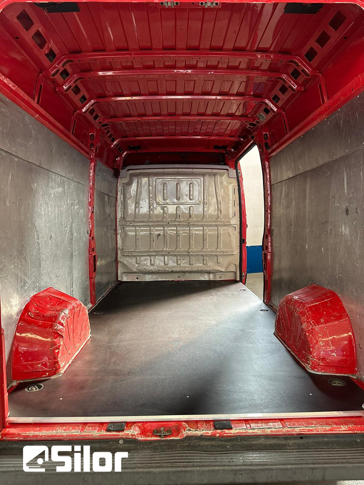Interno di un furgone rosso con pavimento nero.