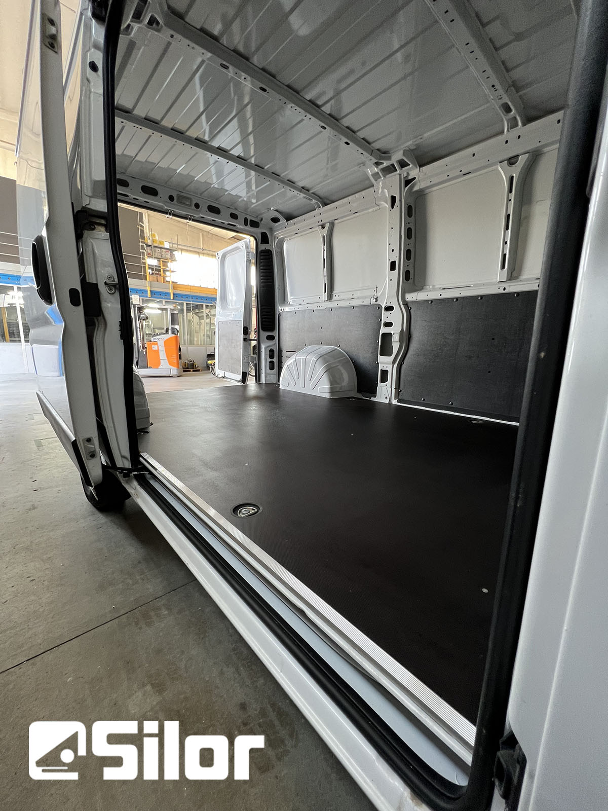 Interni di un furgone con pavimento nero e pareti bianche.