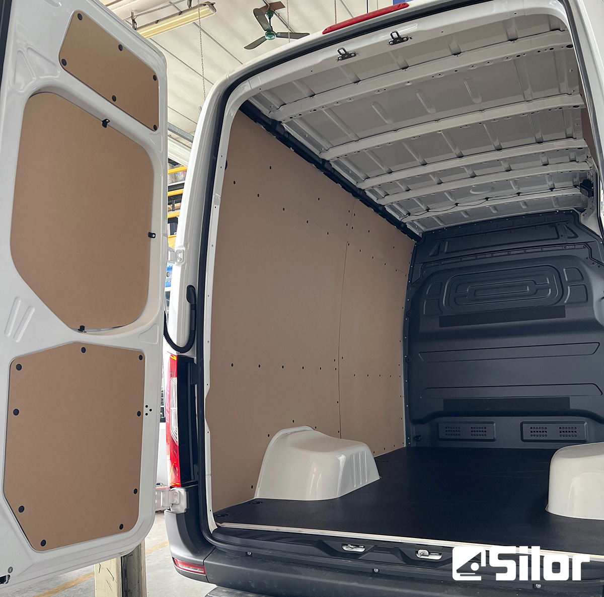 Interno di un furgone bianco con pannelli marroni e pavimento nero.