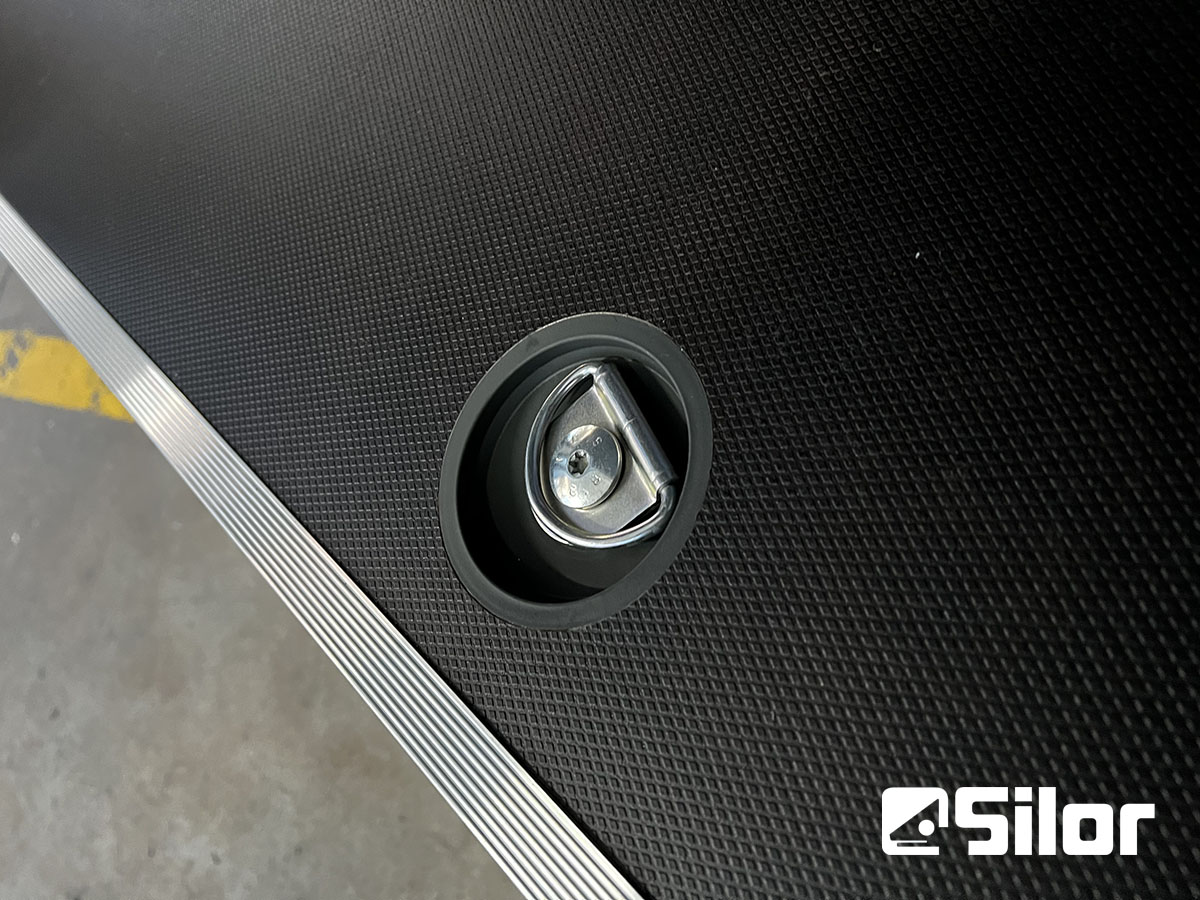 Primo piano di un dispositivo di fissaggio a D su una superficie ruvida nera con finiture metalliche e il logo Silor.