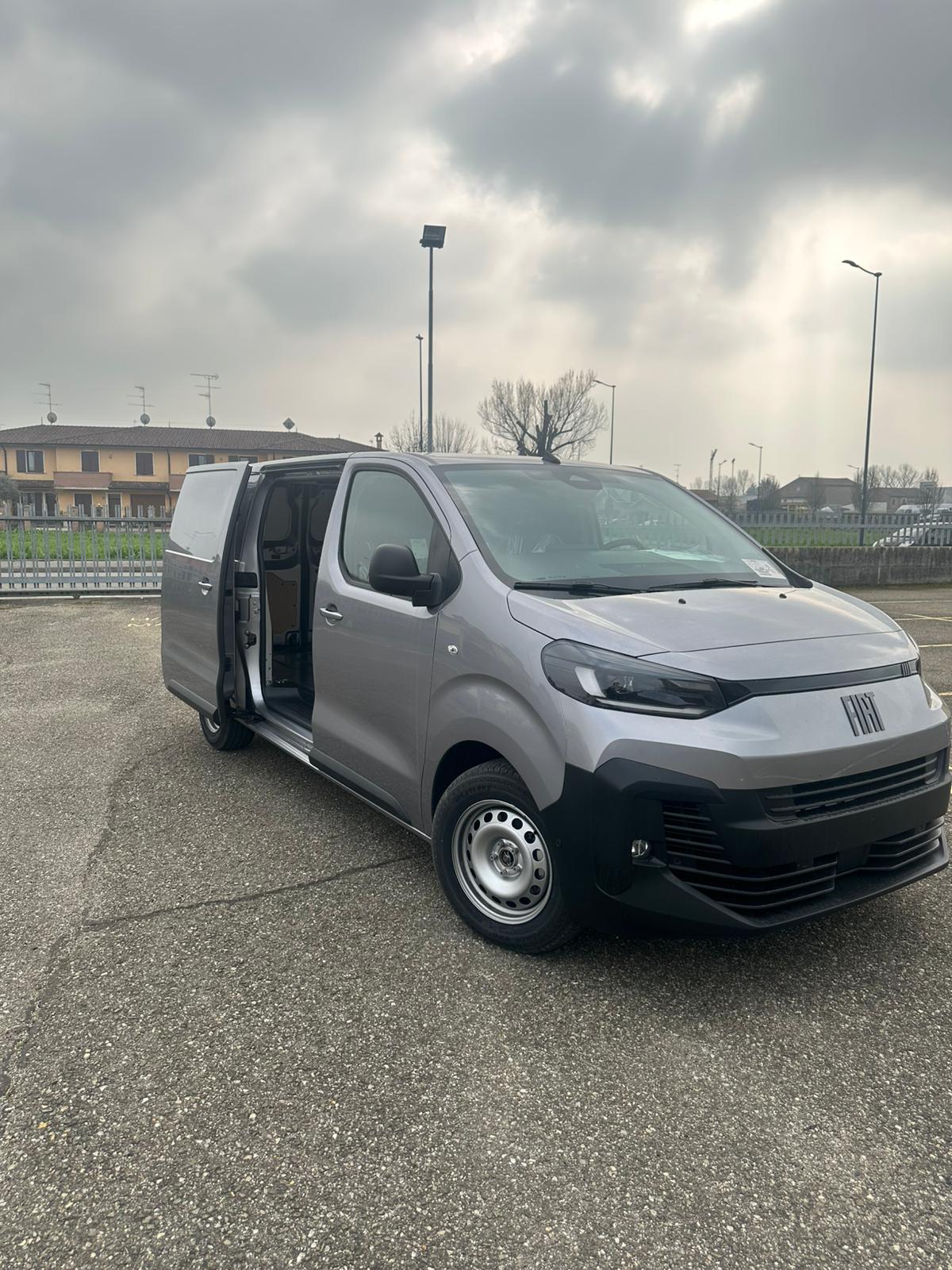 Un furgone Fiat grigio parcheggiato in un parcheggio con le portiere aperte.