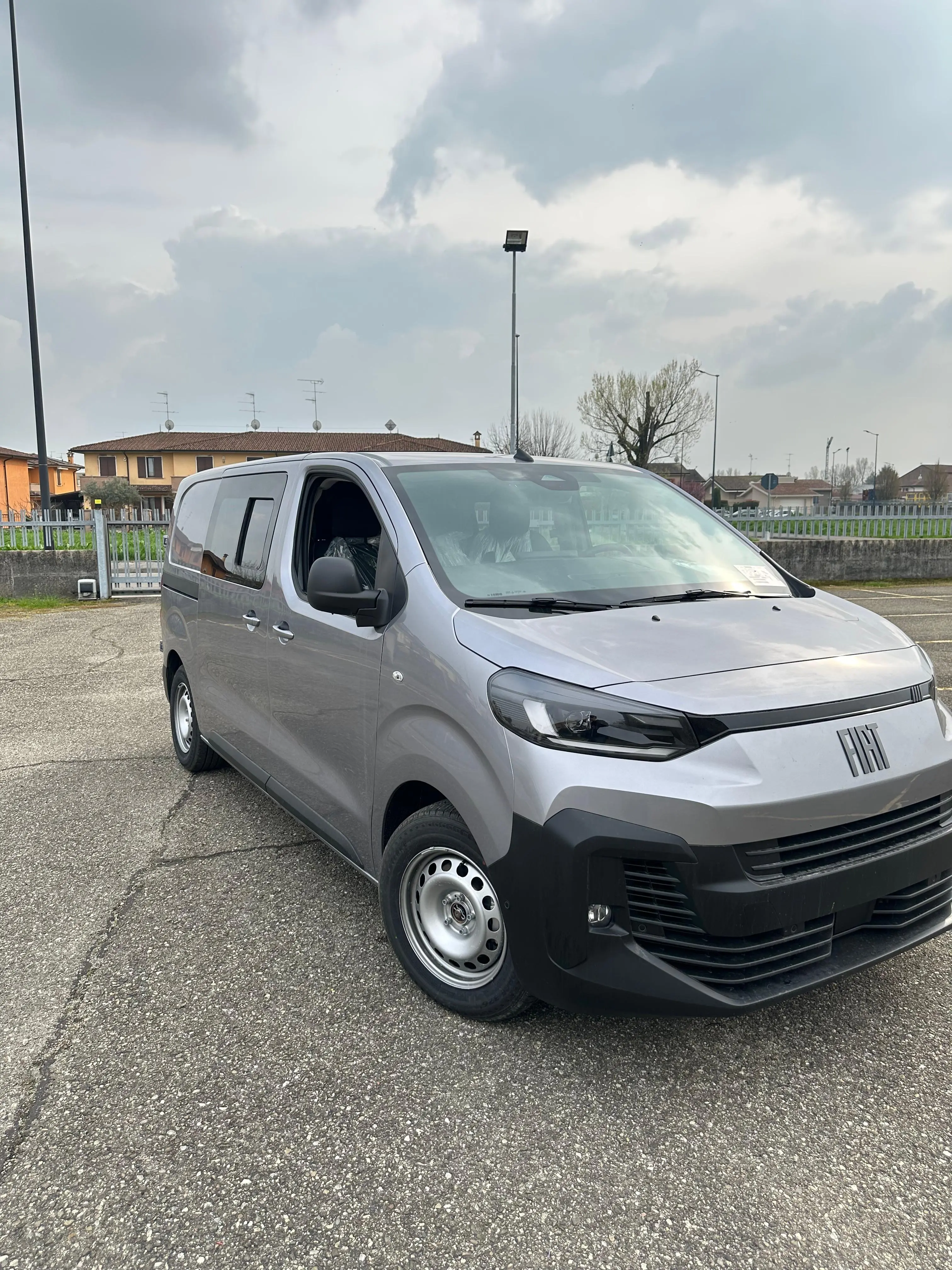 Un furgone Fiat grigio chiaro è parcheggiato in un parcheggio.