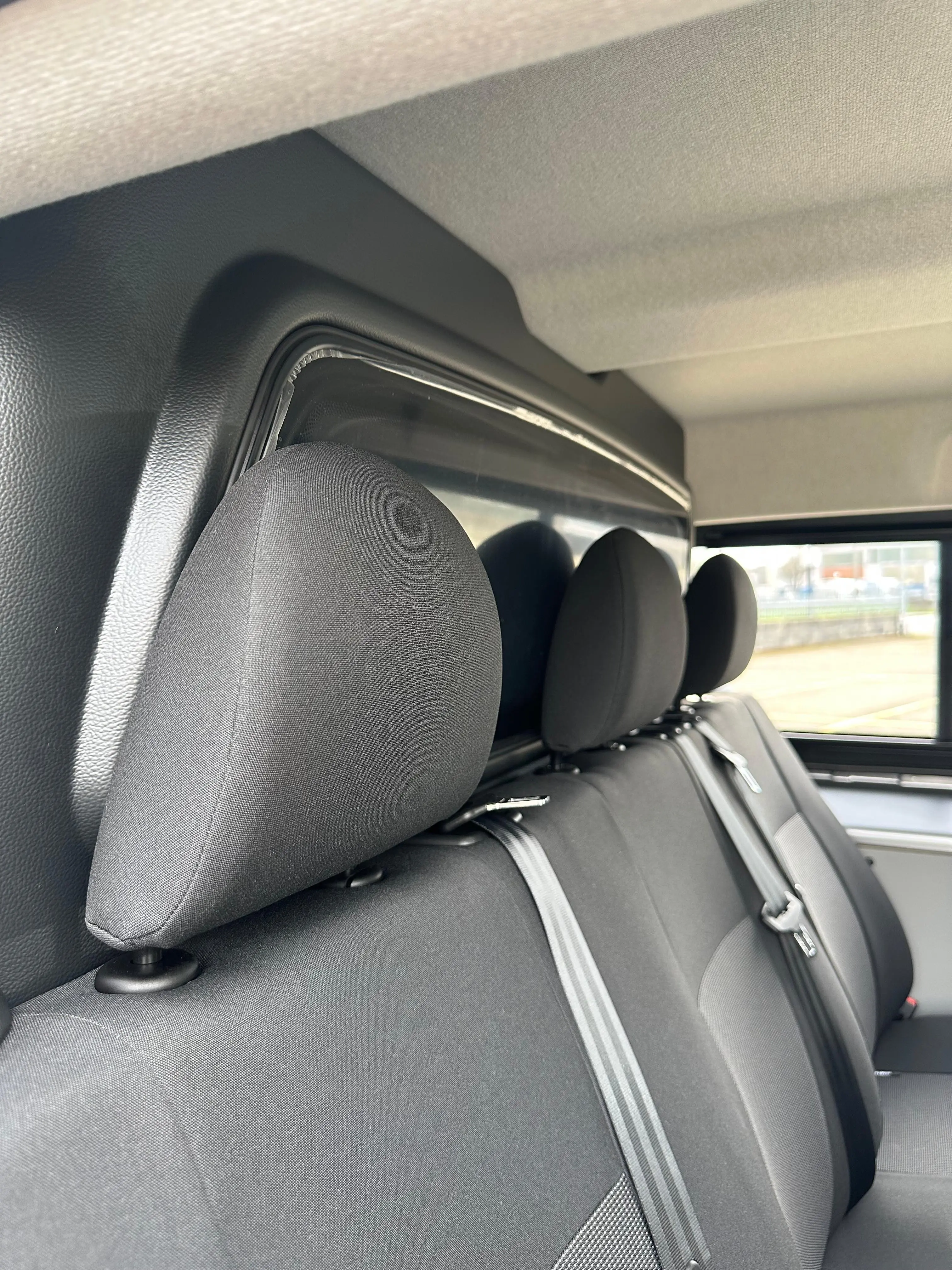 Tre sedili in tessuto grigio con cinture di sicurezza e poggiatesta neri sono visti dall'interno di un veicolo.