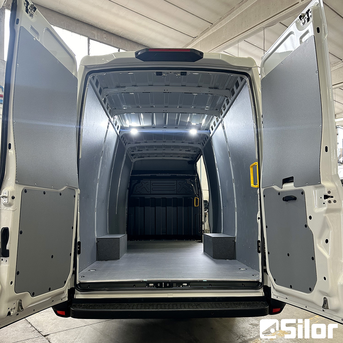 Interno di un furgone bianco con porte posteriori aperte e imbottitura grigia.