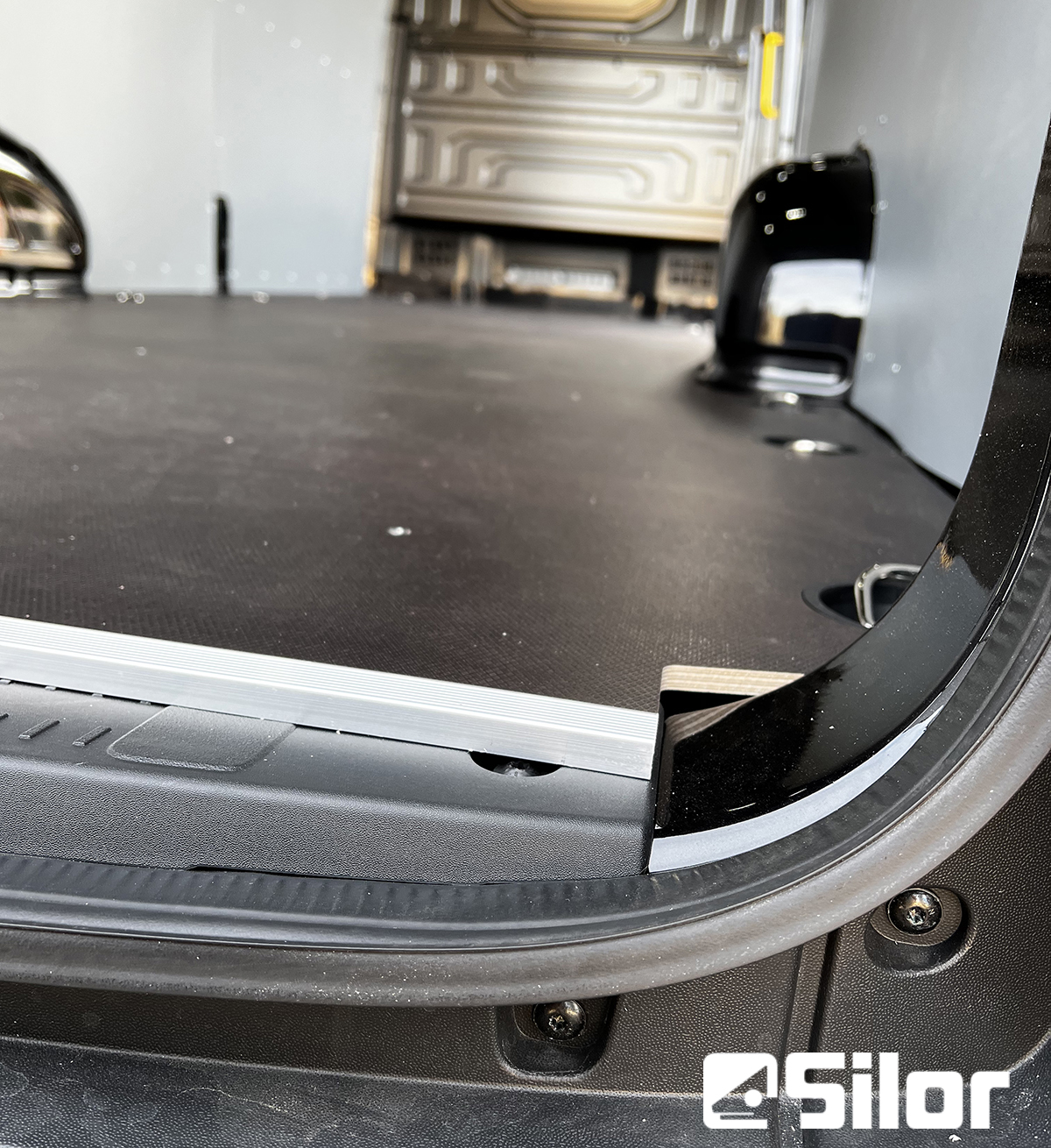 Interni di un furgone con pavimento nero e pareti grigie.