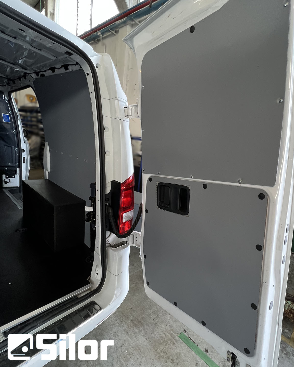 Interni di furgone bianco con pannelli grigi sulle porte posteriori e logo Silor.