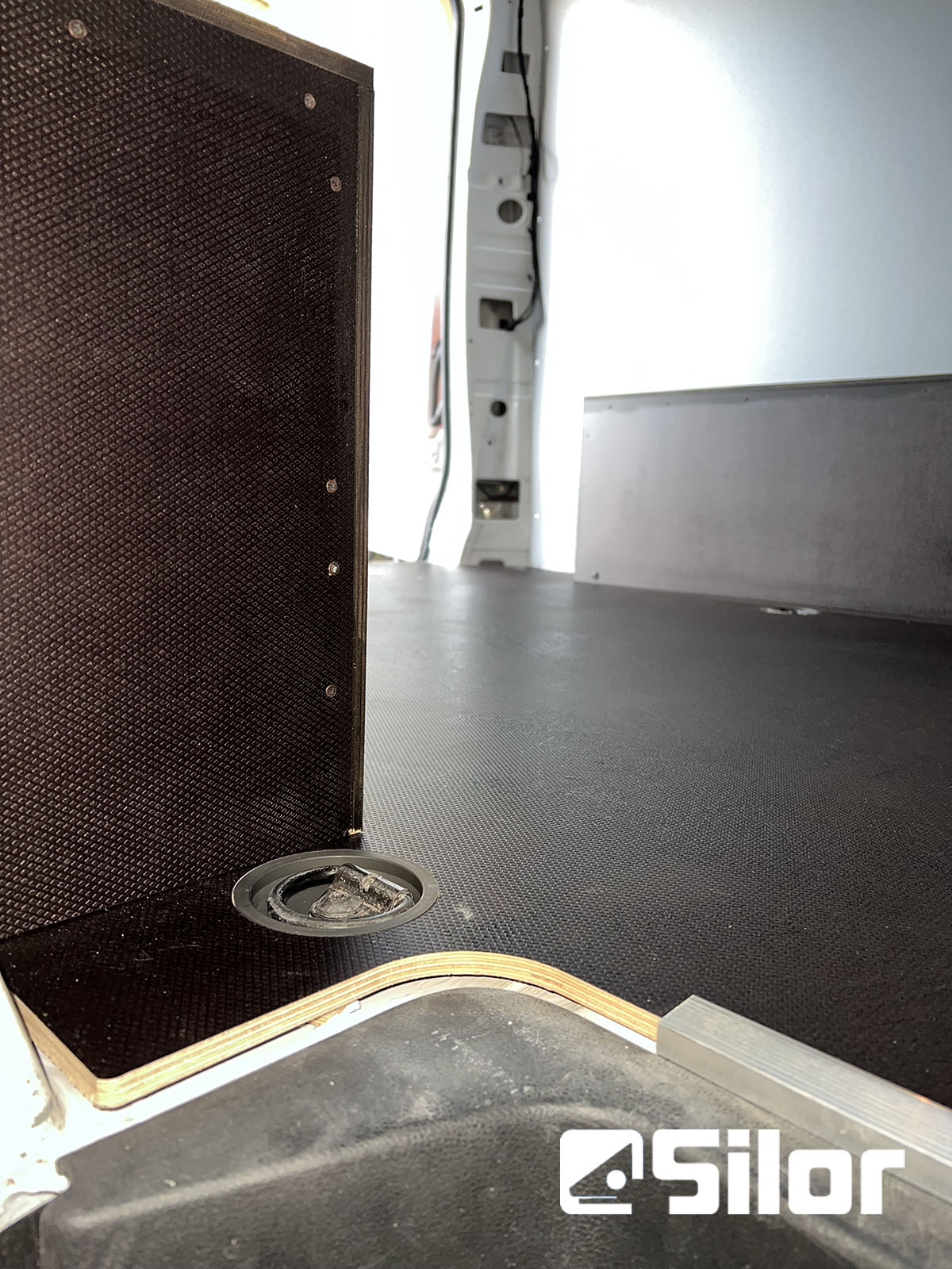 Interni di un furgone con pavimento nero e rivestimento marrone scuro.