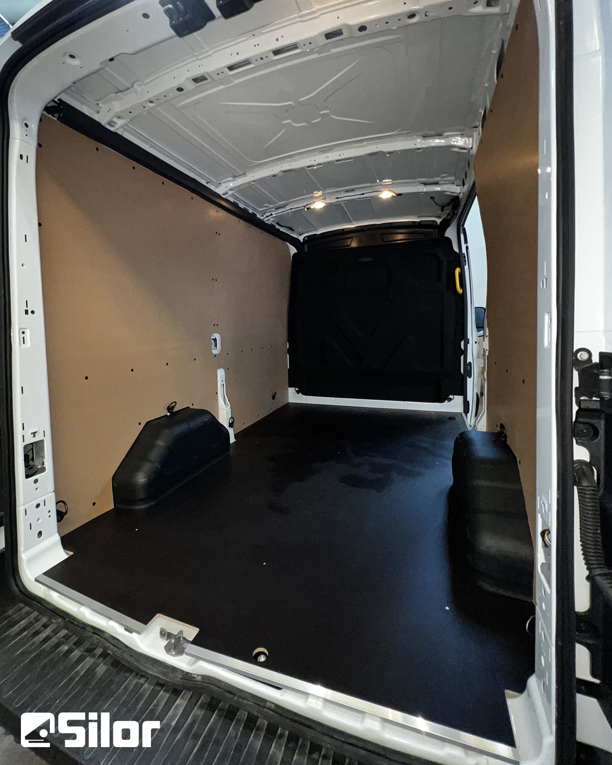 Interni di un furgone bianco con pavimento e pareti marroni.