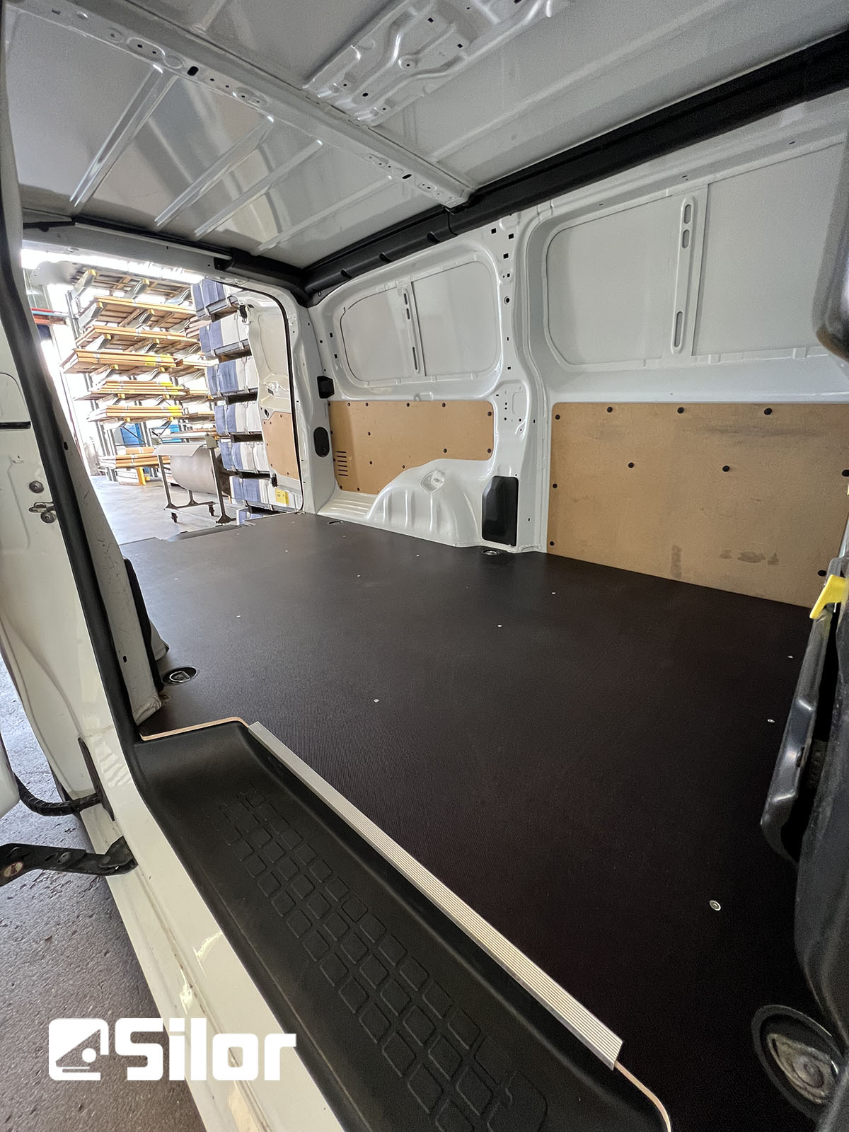 Interni di furgone allestiti con pavimento in legno nero e rivestimento protettivo sulle pareti.