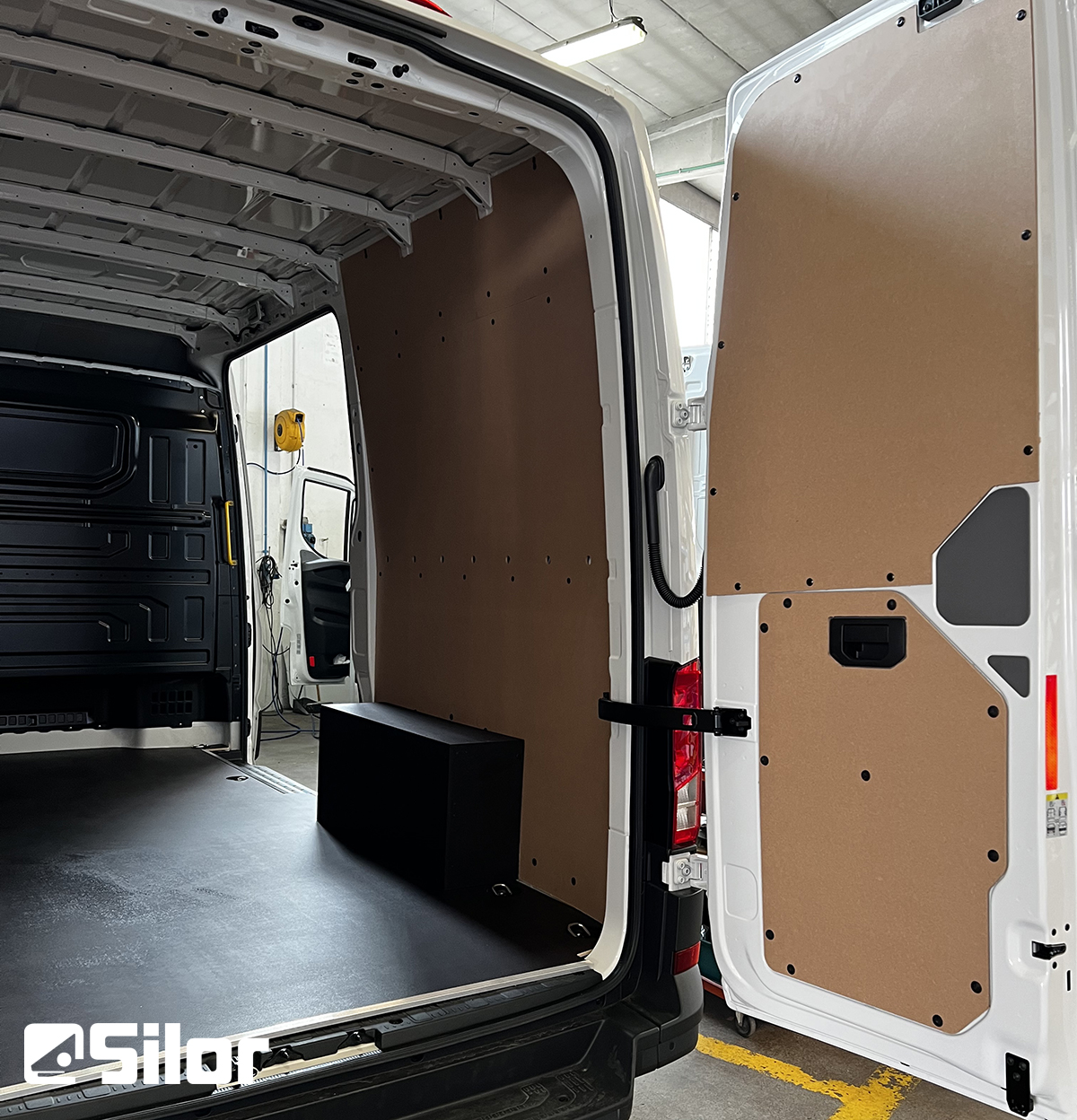 Interni di un furgone bianco con pannelli in legno e pavimento nero.