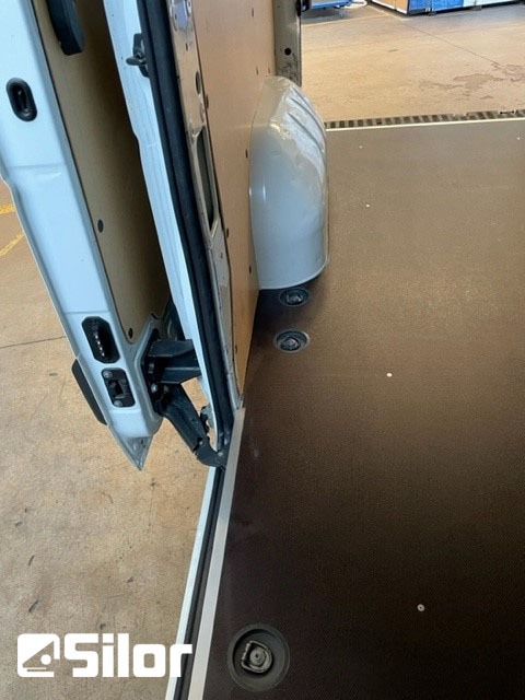 Interno di un furgone bianco con porte aperte e pavimento nero.