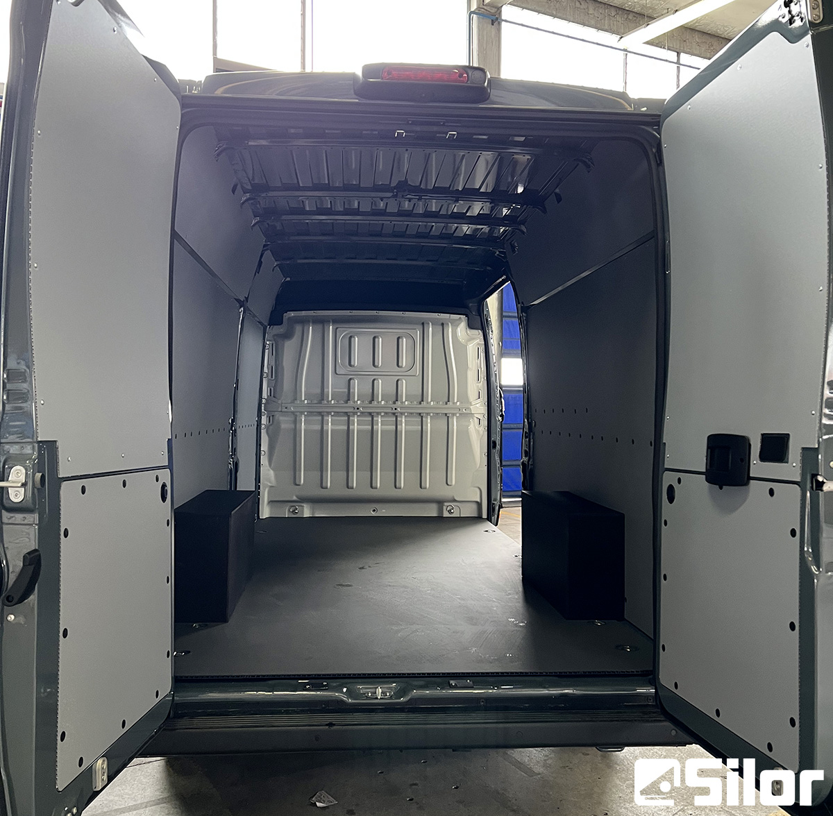 Interni di un furgone merci grigio con due contenitori neri.