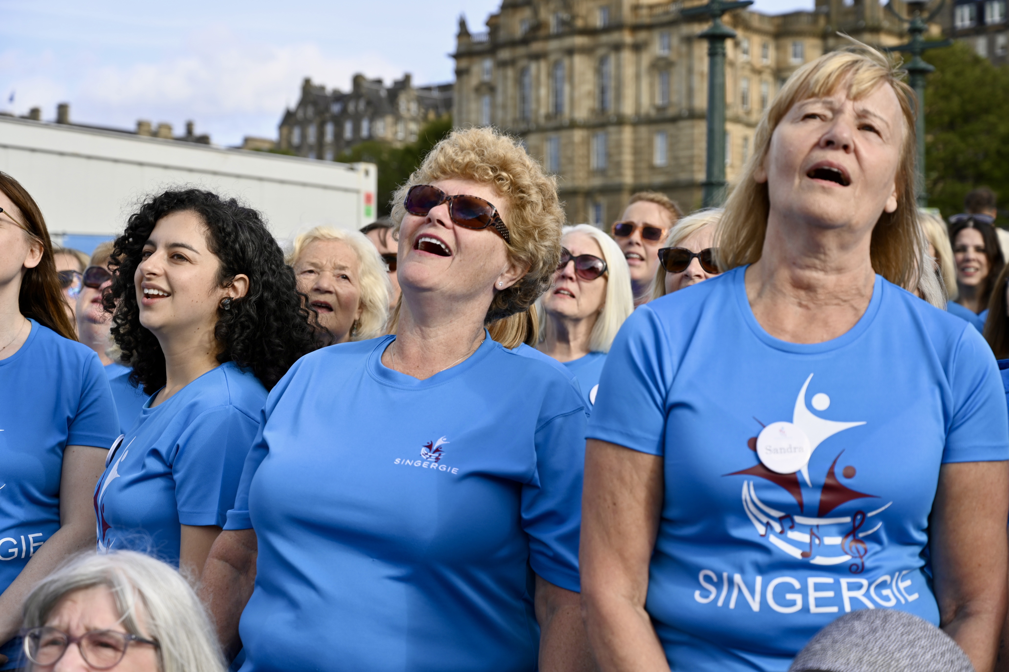 A diverse group of adults smiling while singing during a relaxed rehearsal