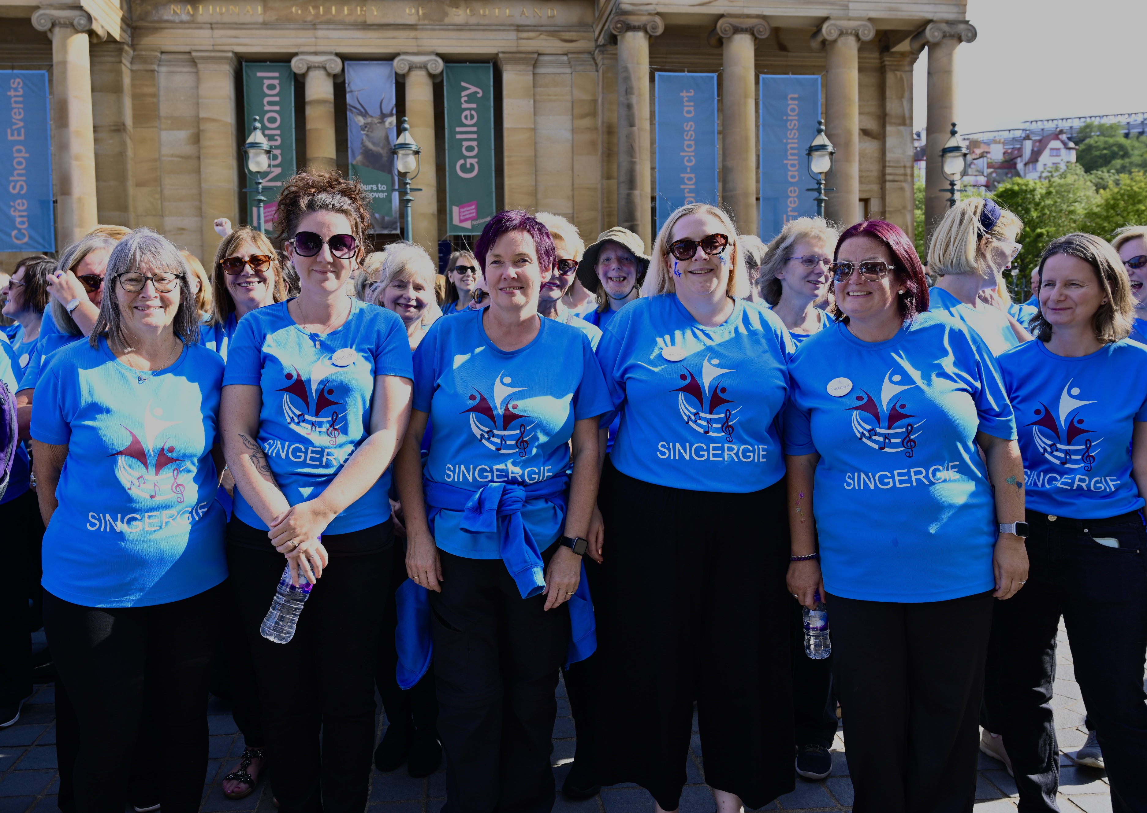 A group of singers in blue Singergie t-shirts standing outdoors