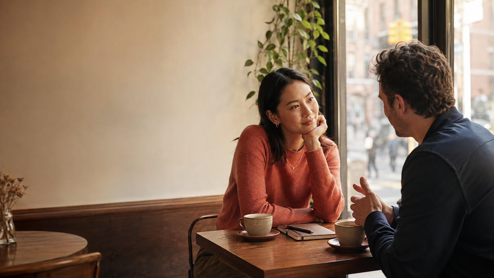 Two people share a thoughtful conversation over coffee during a relaxed first date in a warm neighborhood cafe.