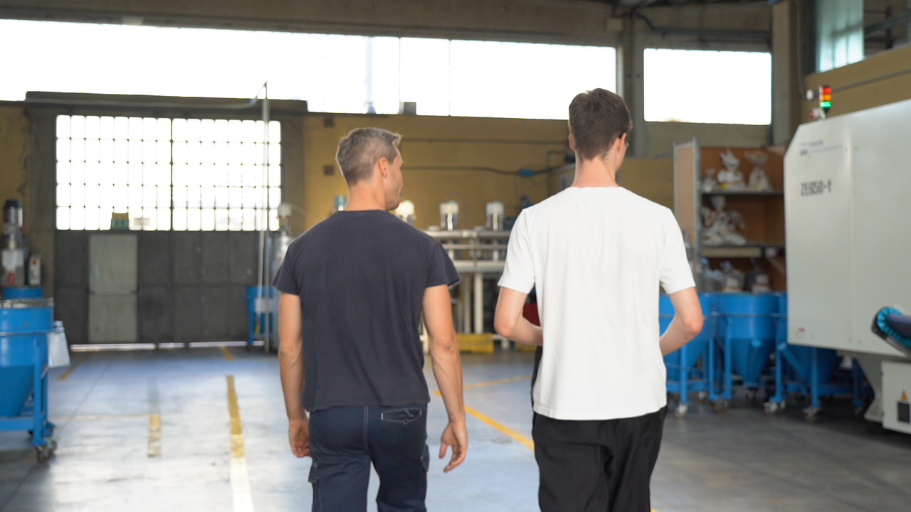 Due uomini camminano in un magazzino.