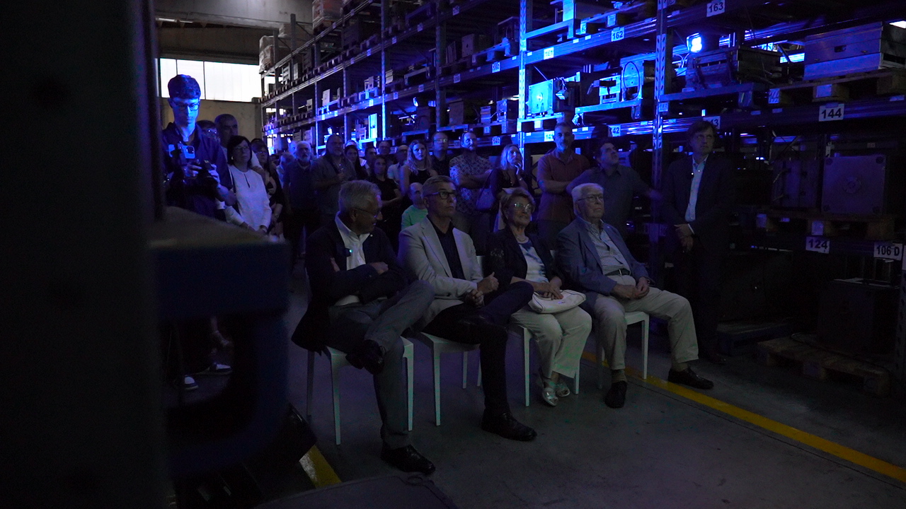 Un gruppo di persone sedute e in piedi in un magazzino.