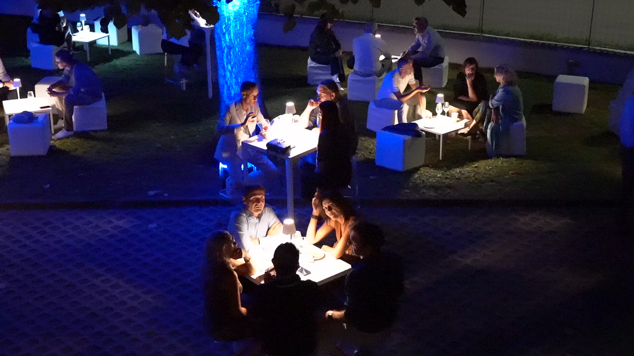 Gente riunita attorno a tavoli illuminati di notte.