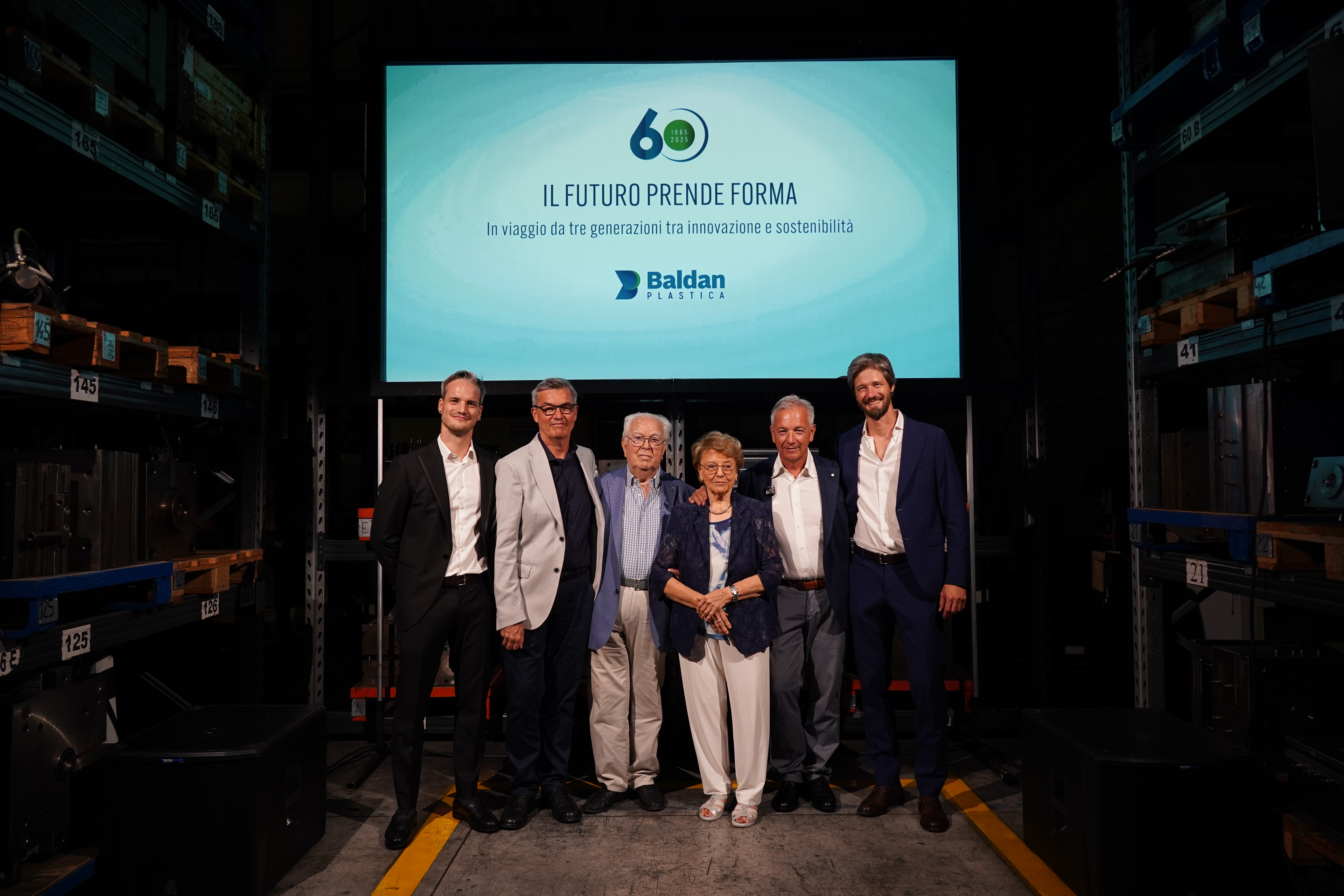 Sei persone posano davanti a un grande schermo con il logo aziendale e lo slogan dell'azienda "Il Futuro Prende Forma".