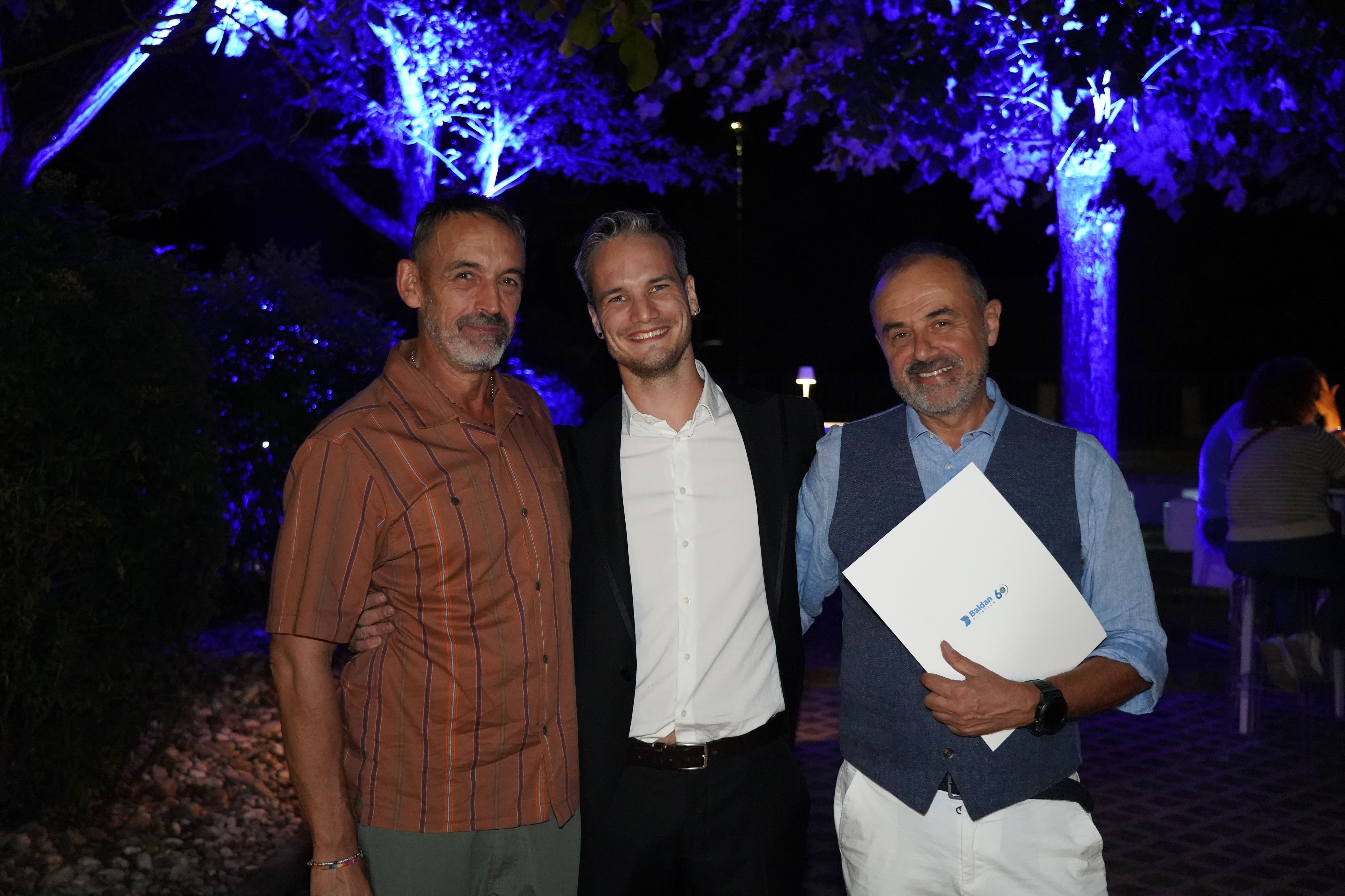 Tre uomini posano per una foto sotto gli alberi illuminati di blu.